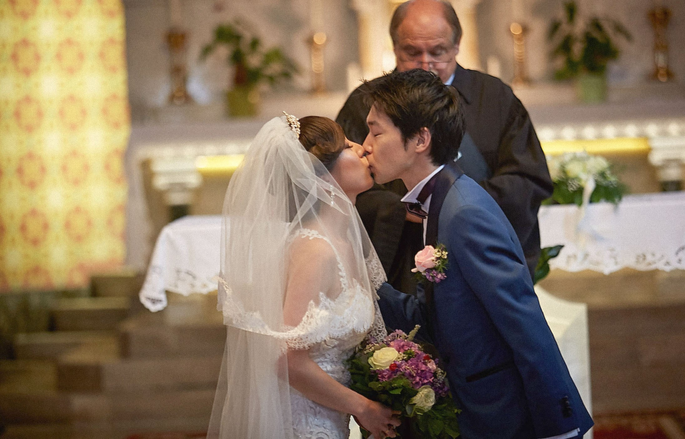 Young Japanese bride and groom kiss at St. Martin's Parish Church, Bled, Slovenia.