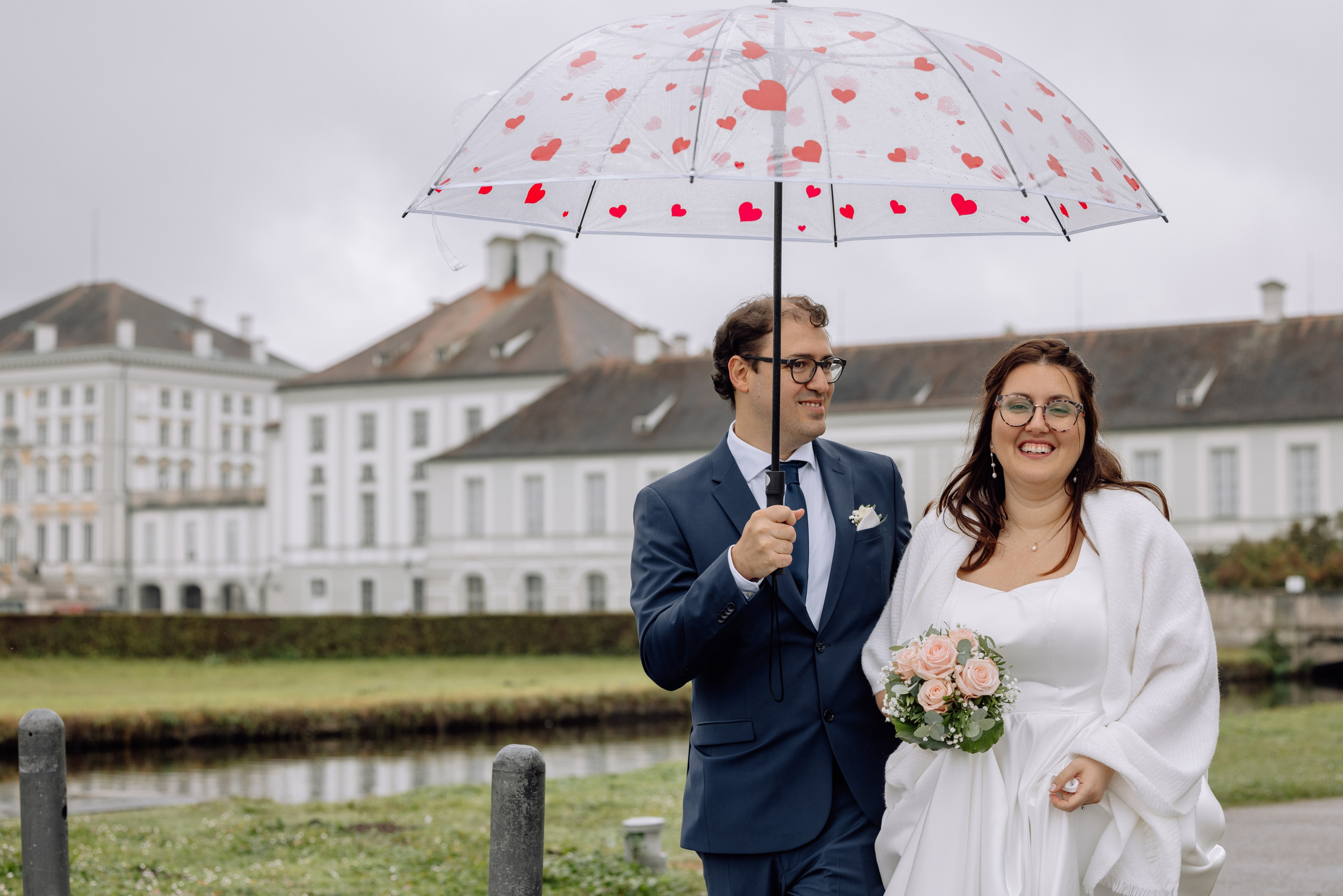 Paar heht unter einem Regenschirm vor dem Schloss Nymphenburg