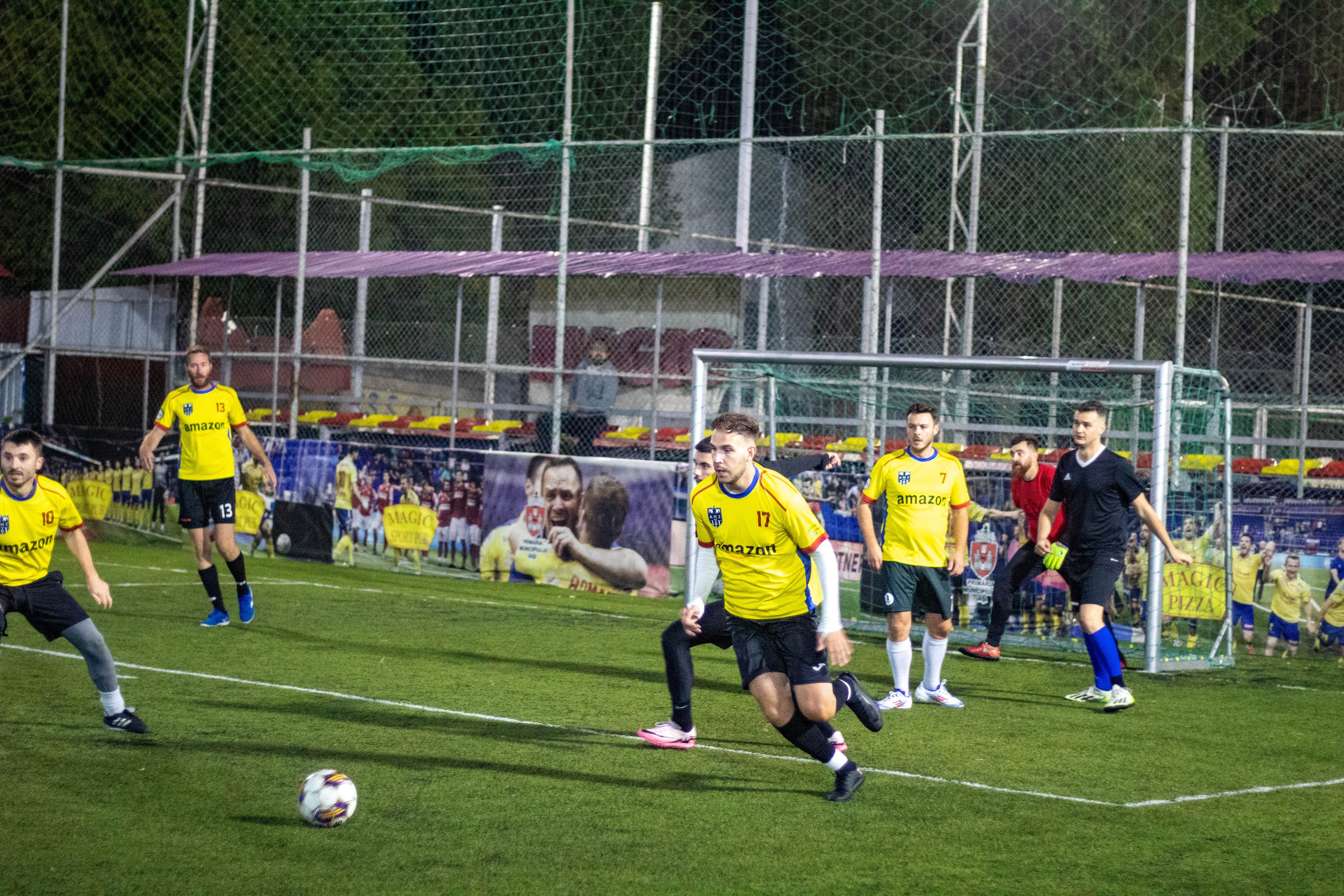 Amateur football match in progress on a green field, players wearing yellow jerseys.