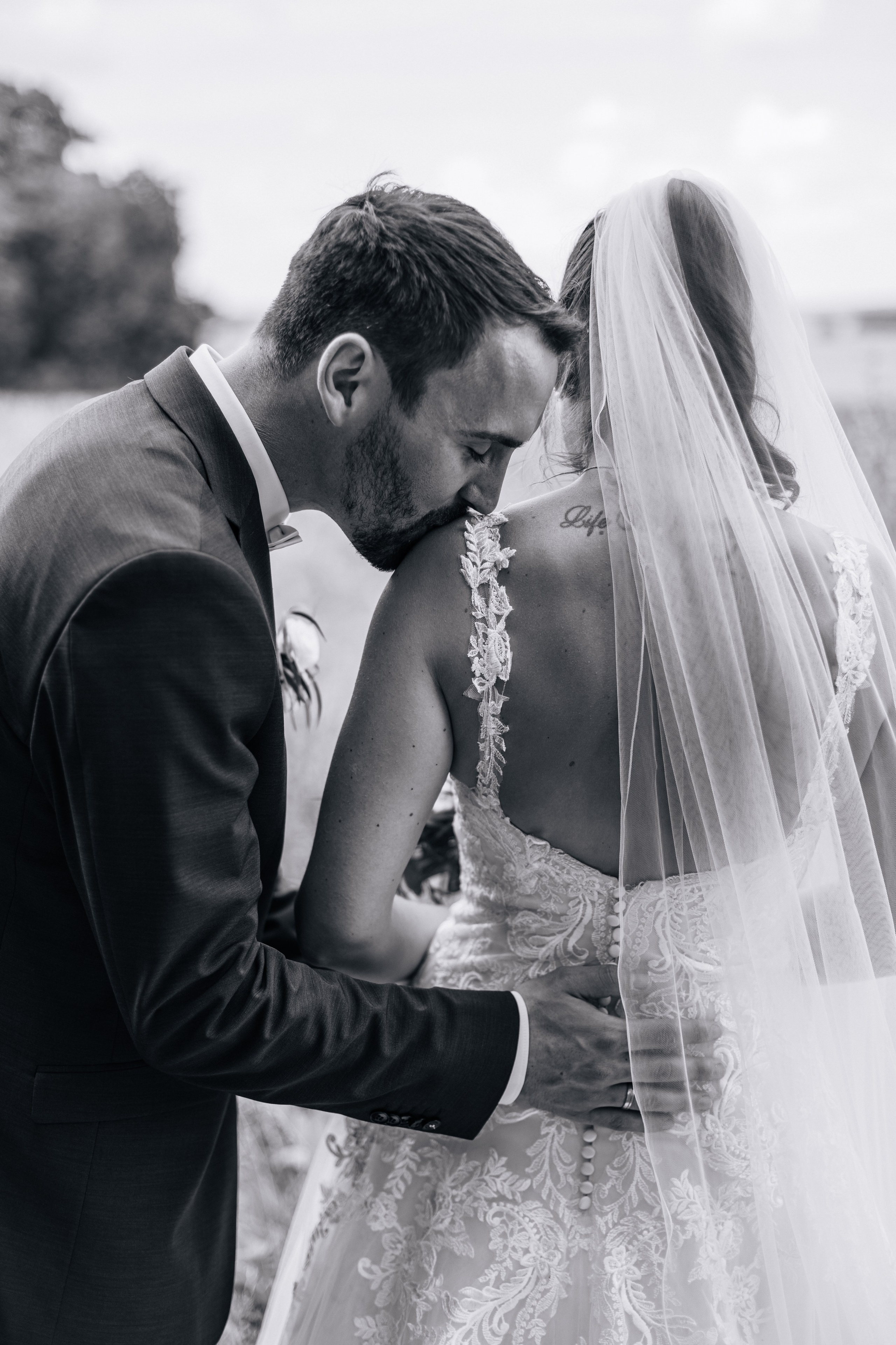 Der Bräutigam küsst die Braut sanft auf die Schulter.