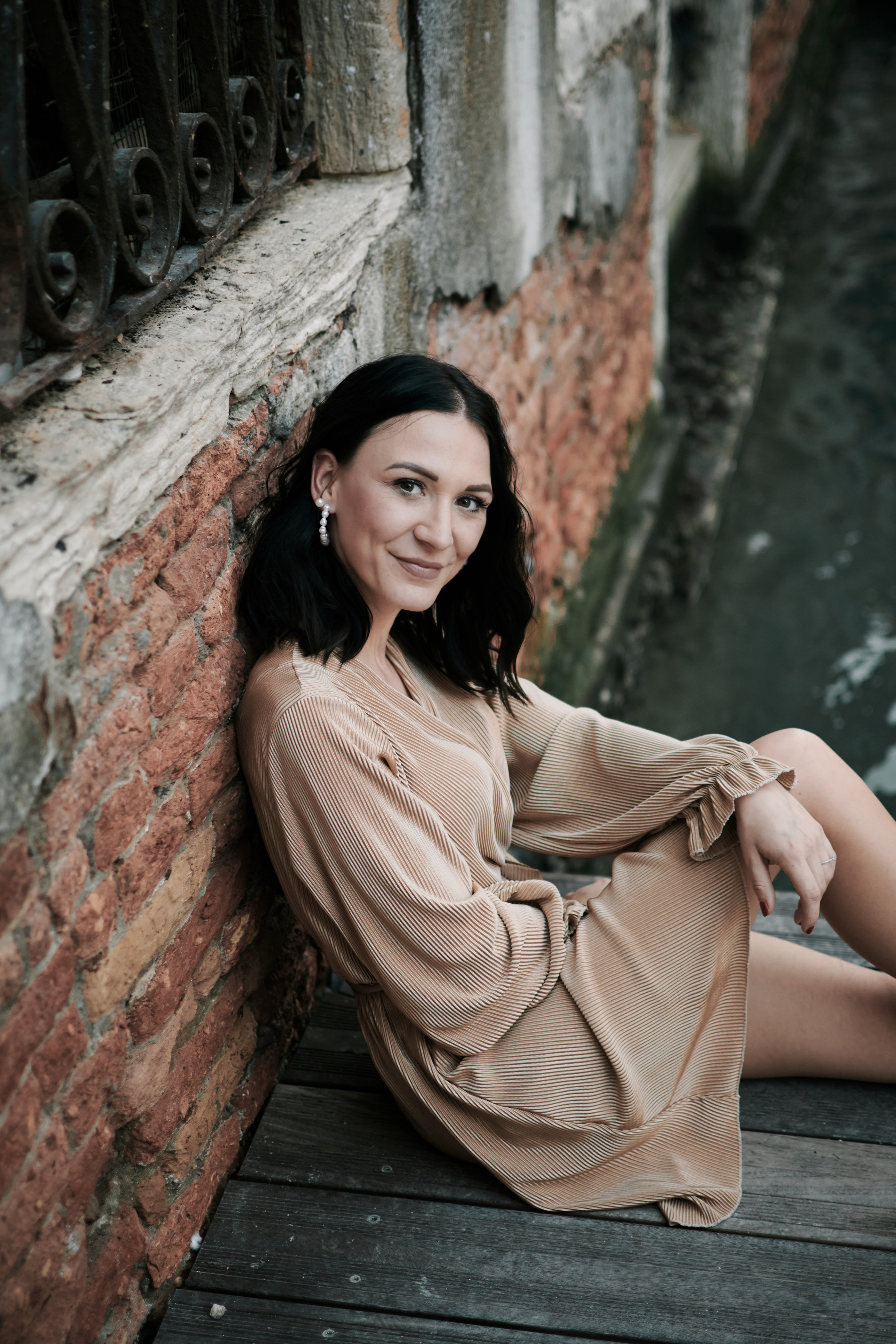 In this portrait photo, a young woman stands on the San Marco square in Venice, her back to the camera. The bustling square lies before her, with people milling about and gondolas drifting along the canal. The woman's pose exudes confidence and independence