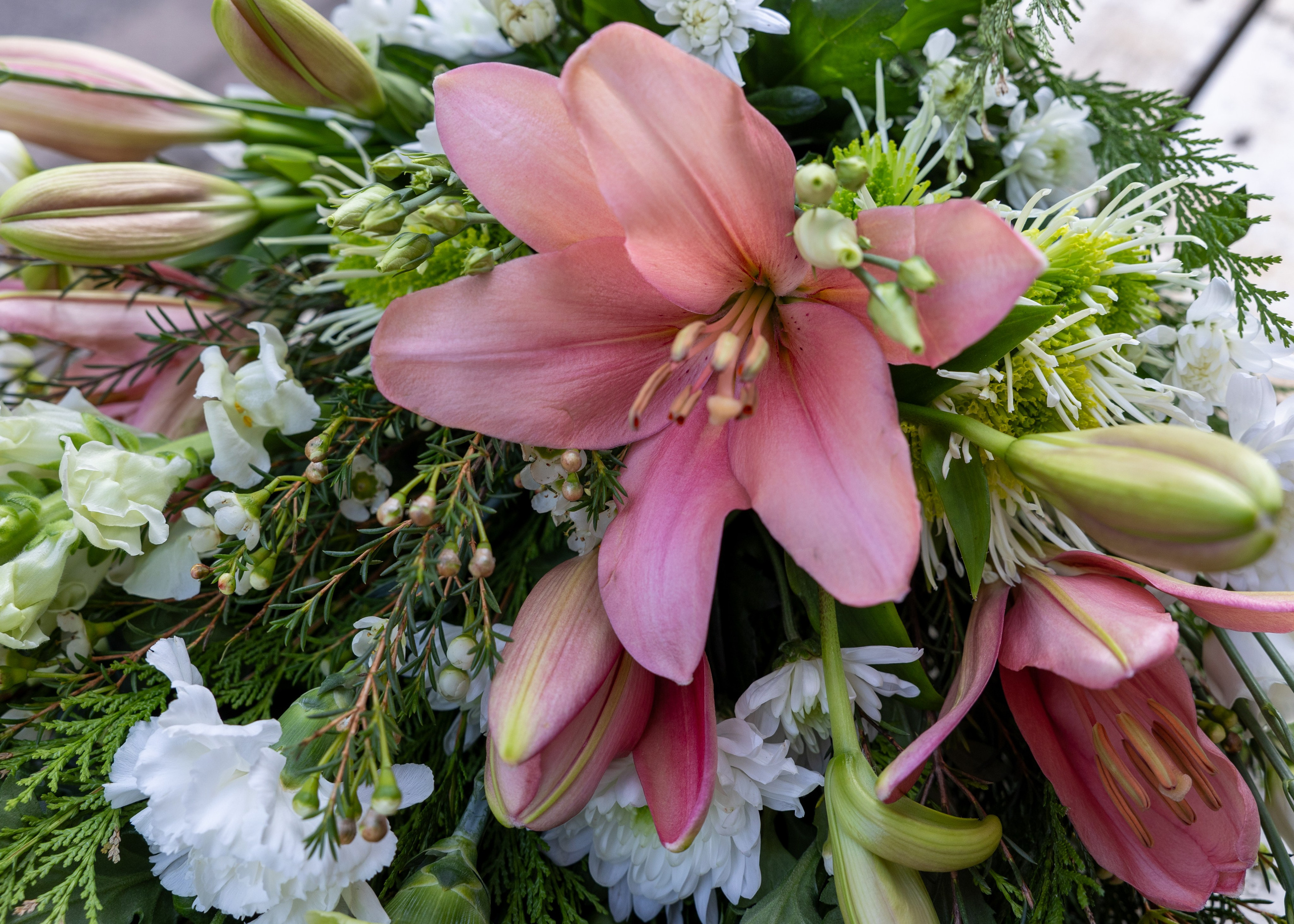 En tidløs bårebuket, hvor blomsterne er tæt bundet i nuancer af lyserød og hvid. Denne klassiske buket passer til alle årstider og udgør en smuk sidste hilsen.