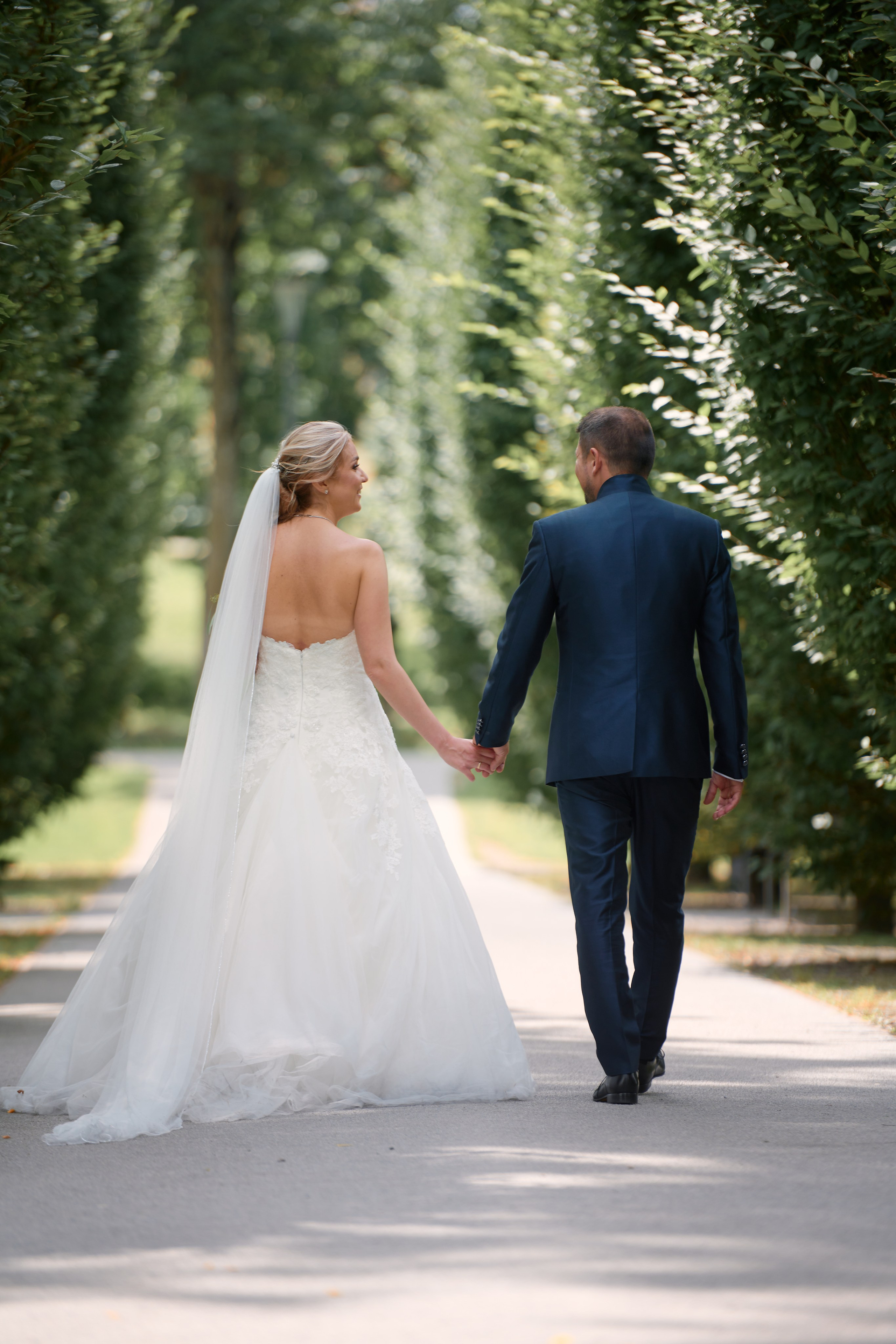 Viktoria & Alex Hand in Hand in Karlsruhe – Brautpaarshooting in einer lichtdurchfluteten Allee, voller Leichtigkeit und Nähe.