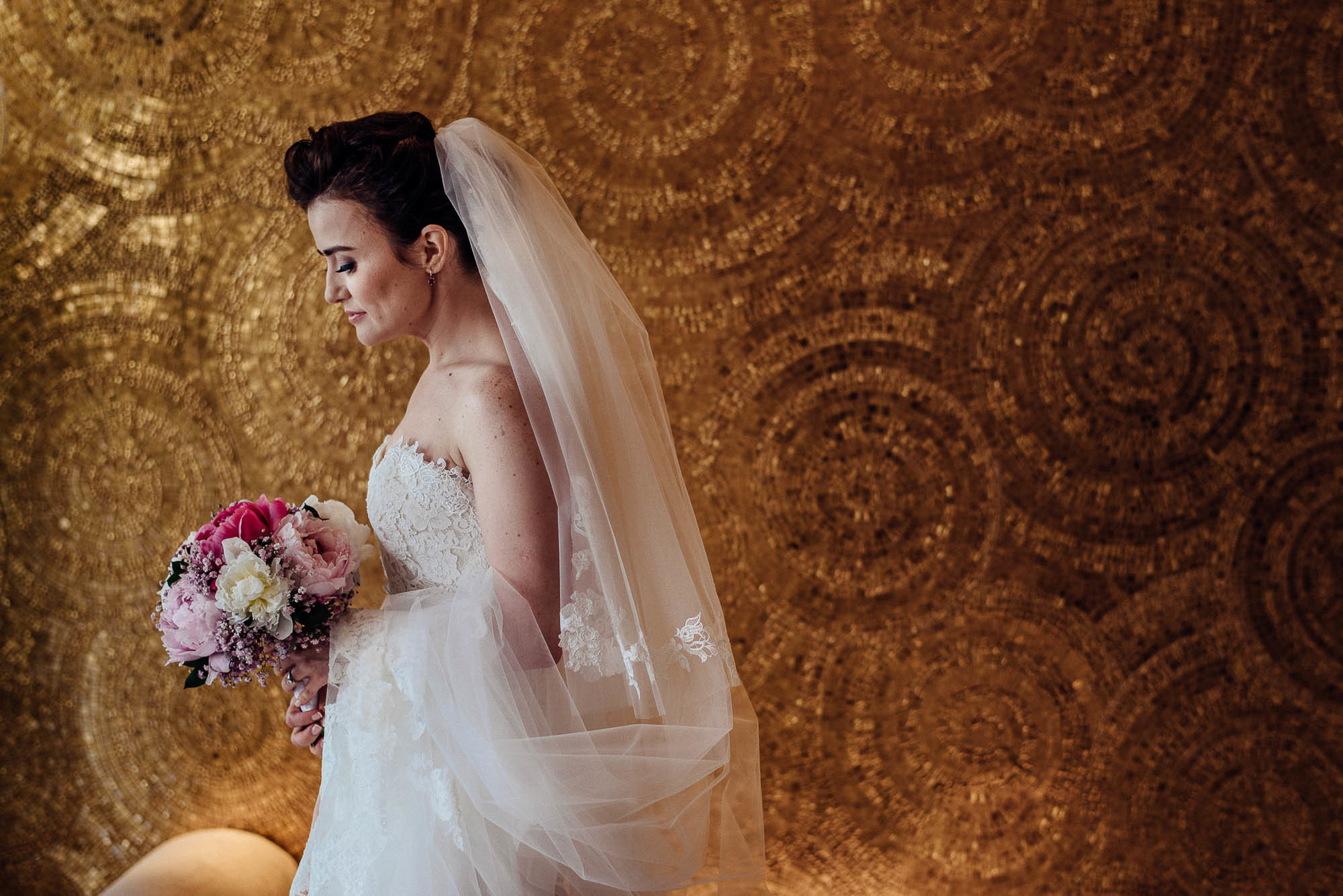 Невеста с букетом цветов в белом платье с фатой на фоне золотой мозаики фотосессия в Дубаи