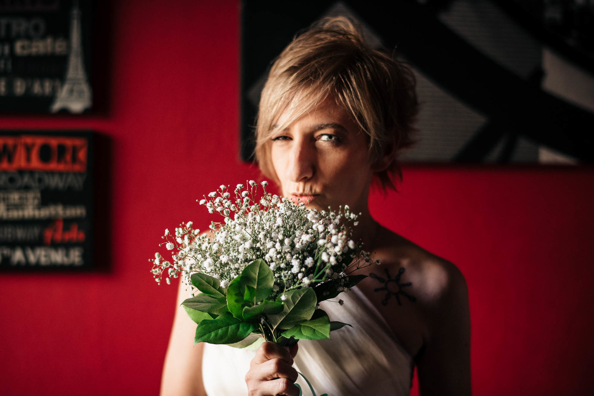 Невеста в белом платье с букетом цветов на фоне красной стены с картинами, свадебный фотограф в Вероне