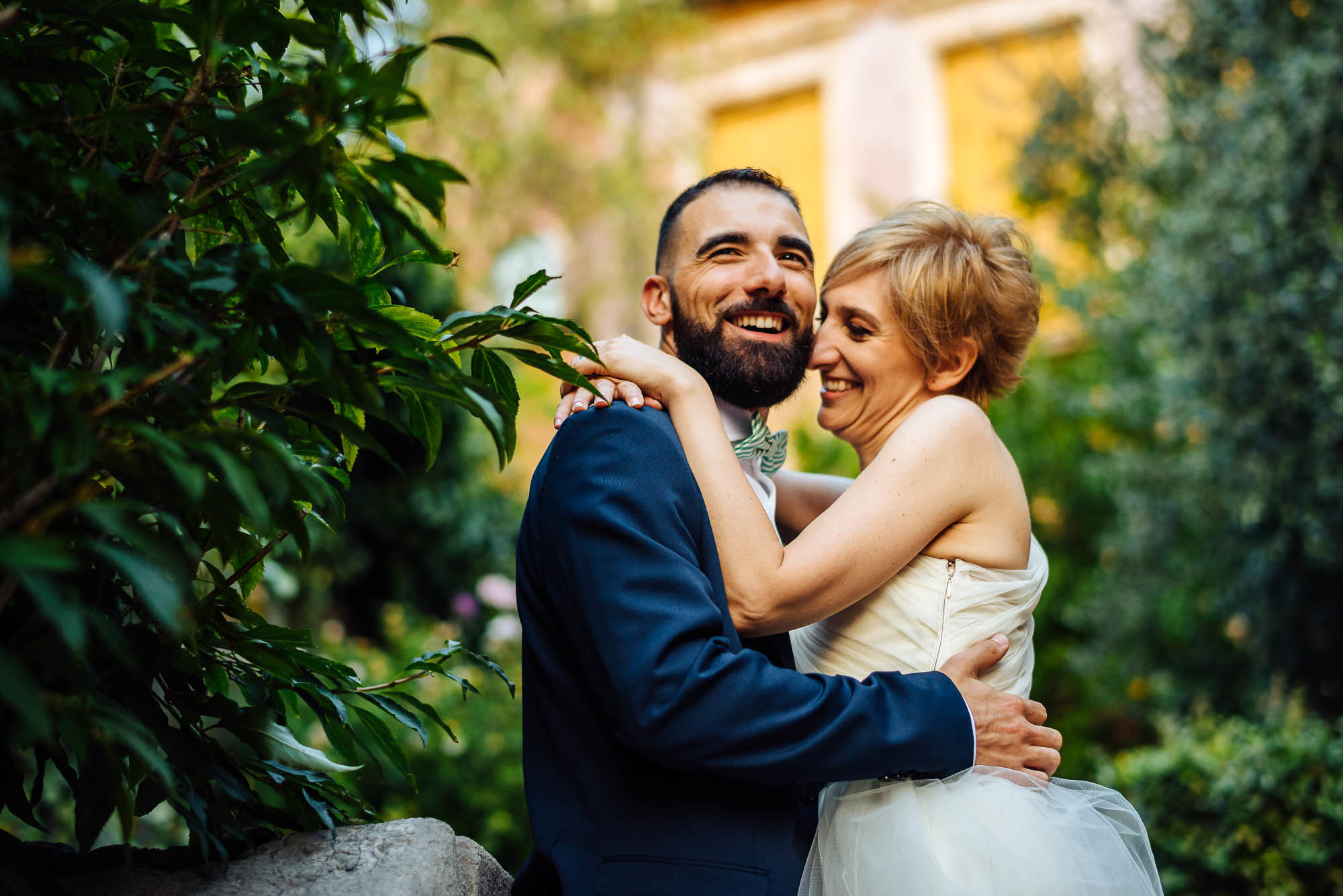Жених обнимает невесту в парке под тенью зеленых кустов, свадебная фотосессия в Вероне
