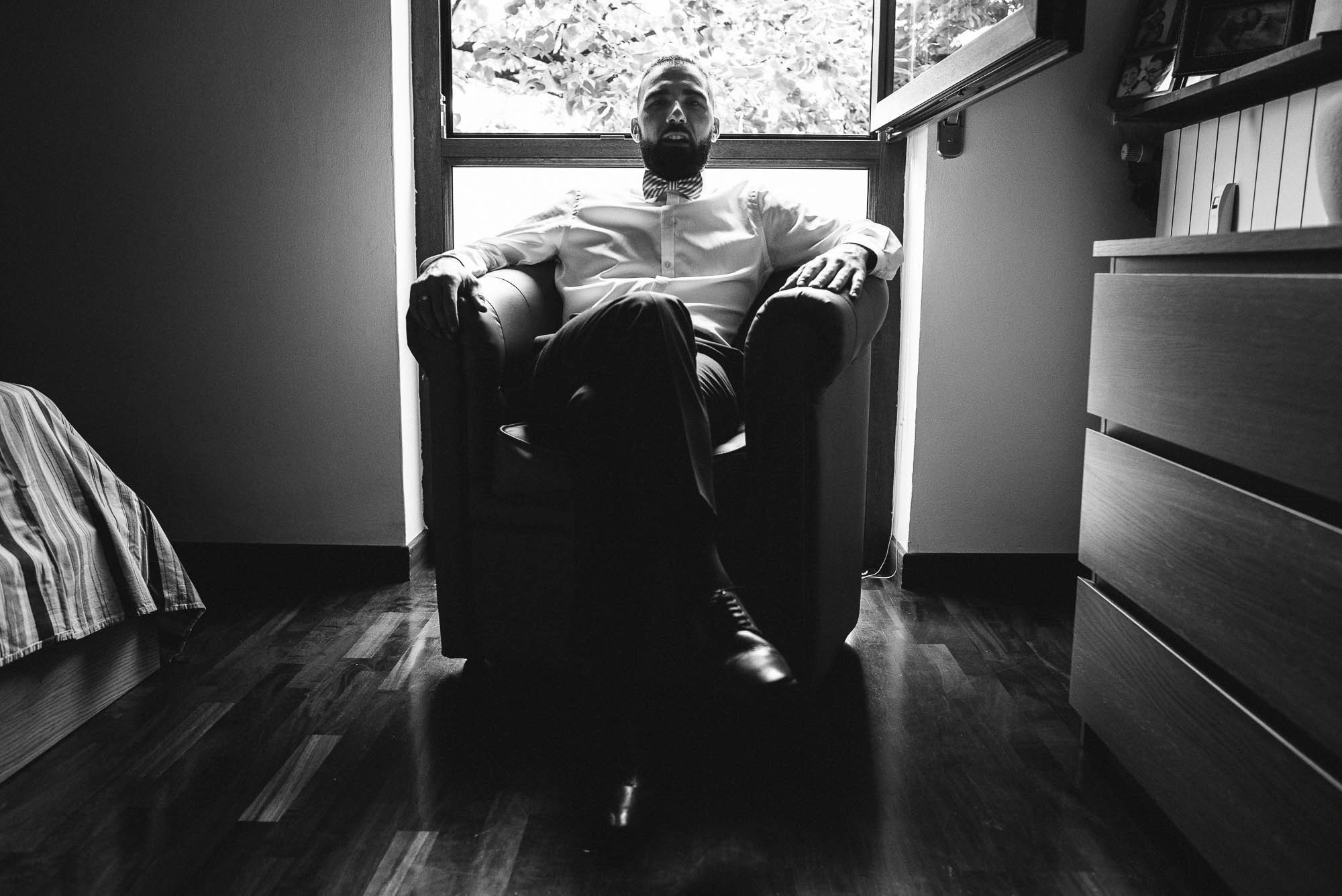 Мужчина во властной позе сидит в кресле спиной к окну, фотосессия перед свадьбой в Италии