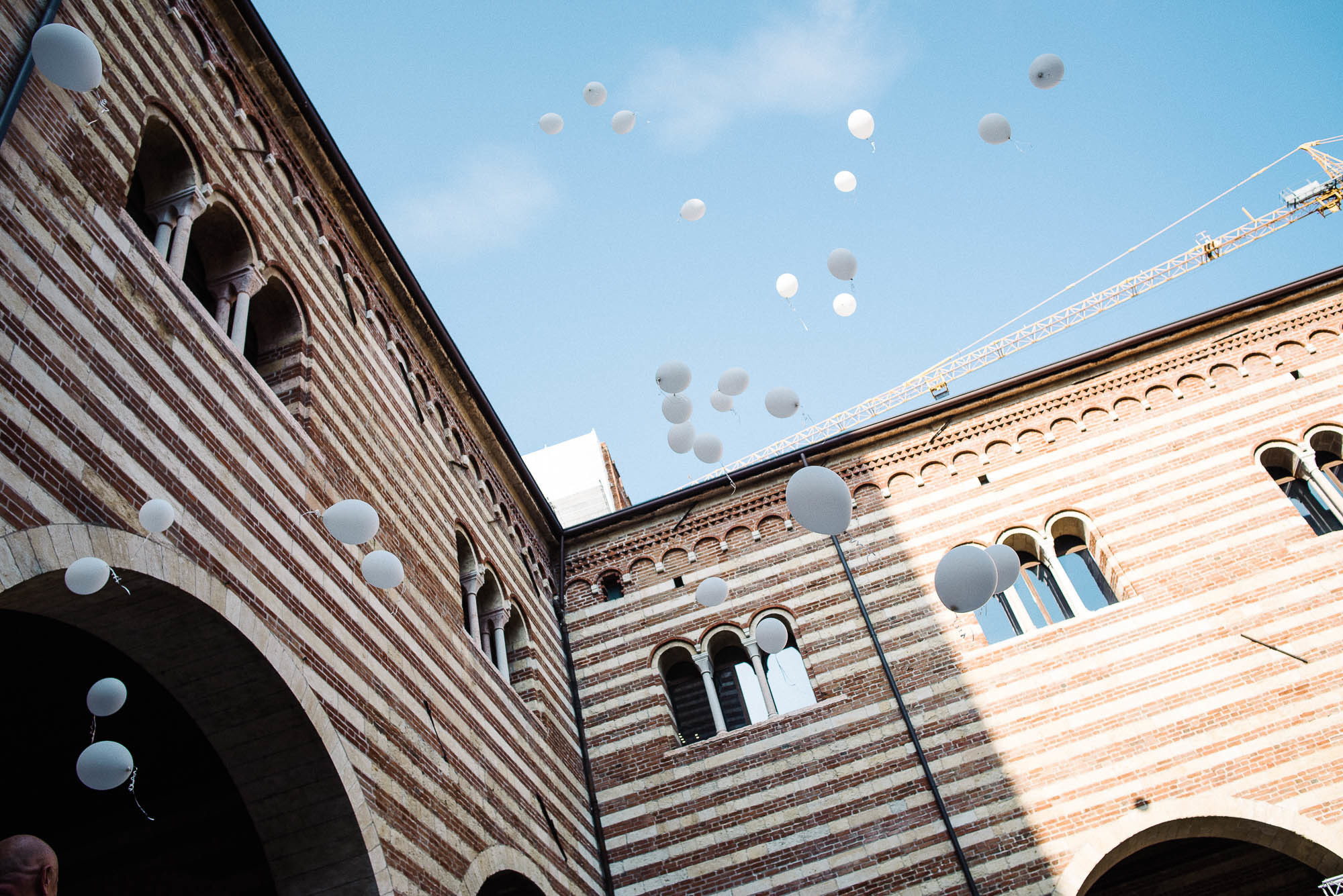 Белые воздушные шарики улетают в небо на фоне старинного здания в Вероне, свадебная фотосессия