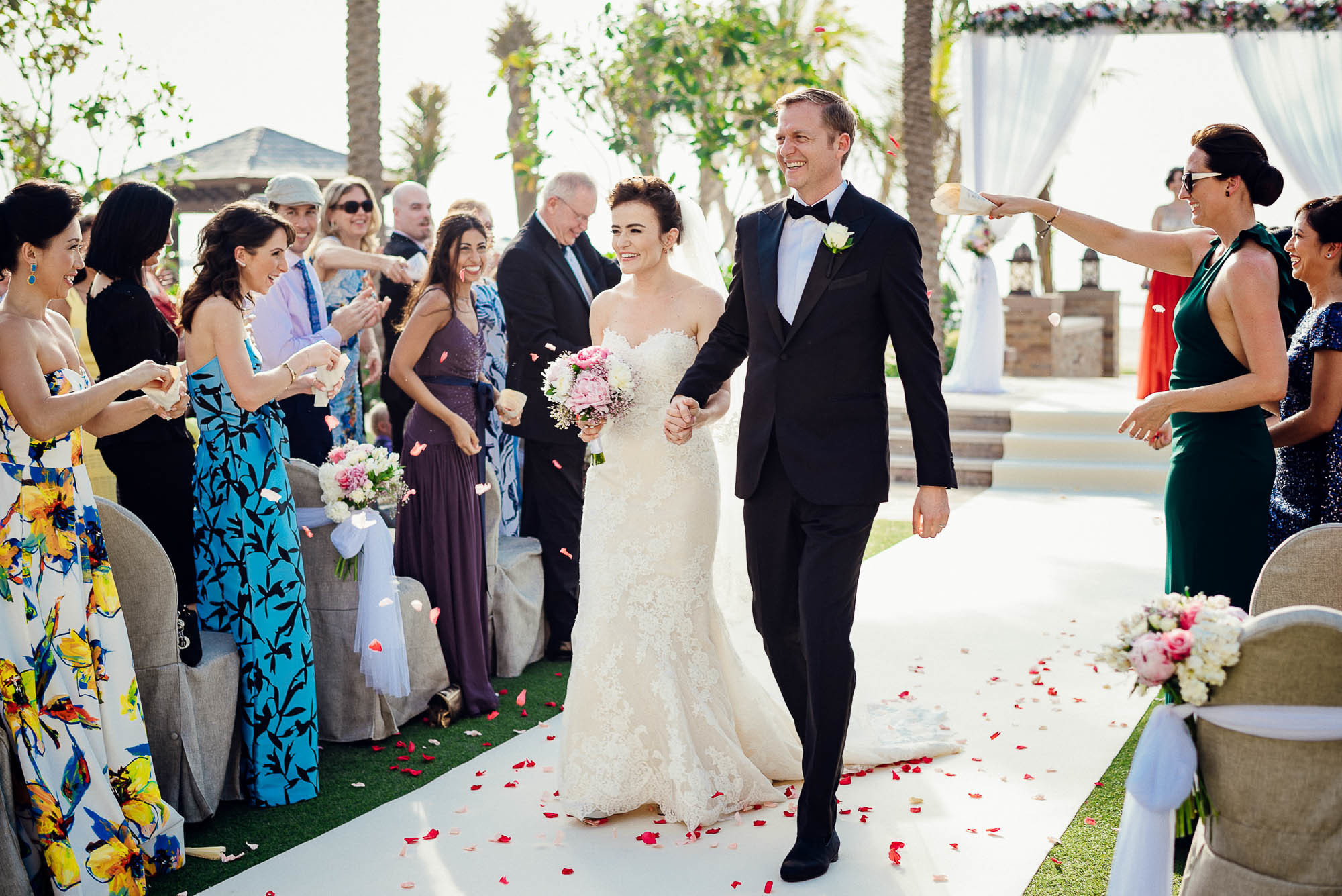 Свежеиспеченные новобрачные идут сквозь гостей, осыпающих их лепестками цветов