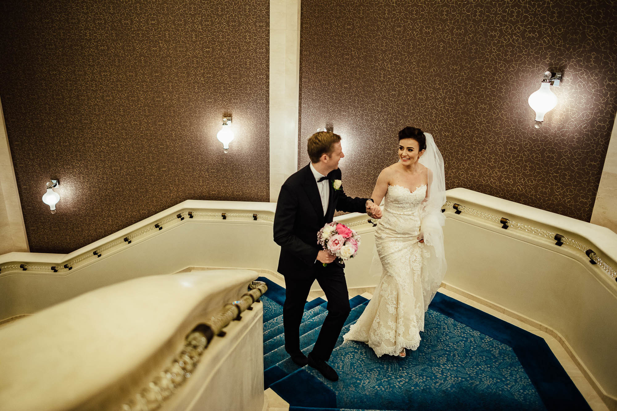 Жених и невеста с букетом цветов держась за руки поднимаются по лестнице во время свадебной фотосессии