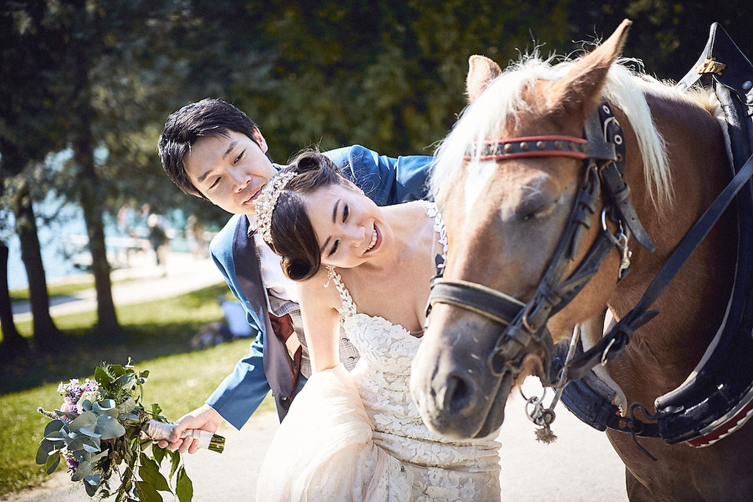 A young Japanese bride gets a closer view of a horse as her smiling groom stands behind her.