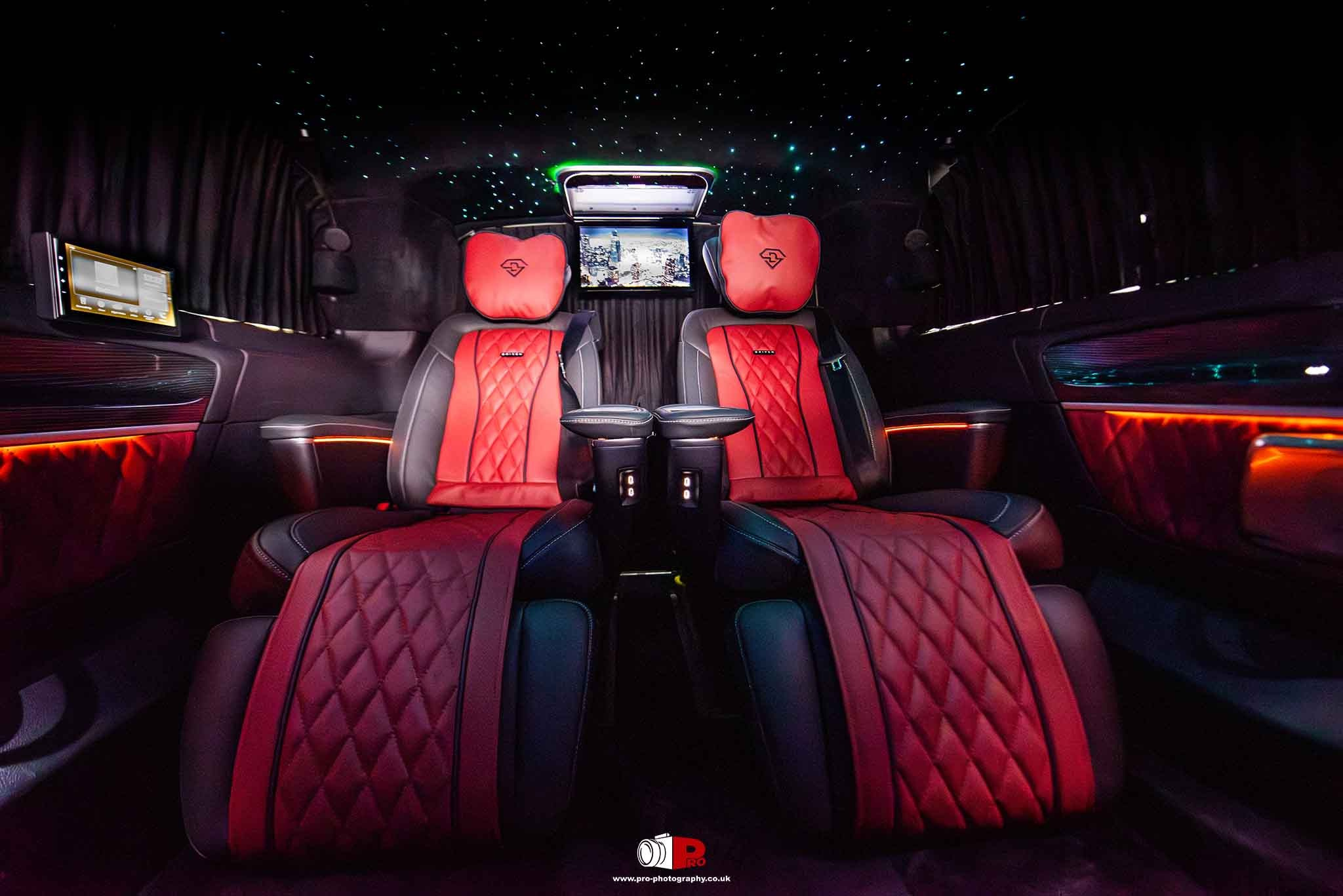 A luxury car's rear interior with vibrant red seats, mood lighting, and advanced entertainment systems.
