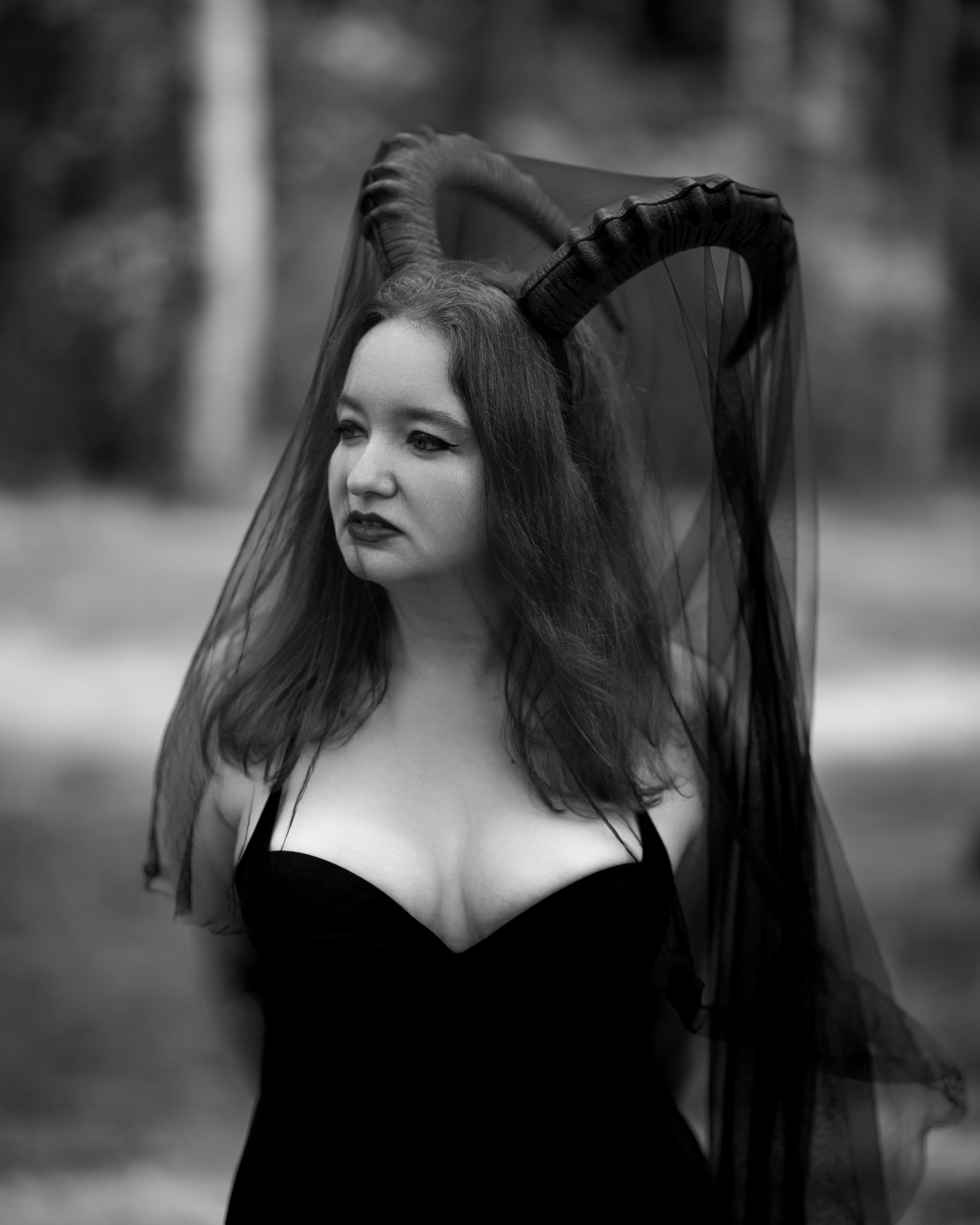 Ksenia steht auf verwurzeltem Waldboden mit Hörnern und tiefem Blick