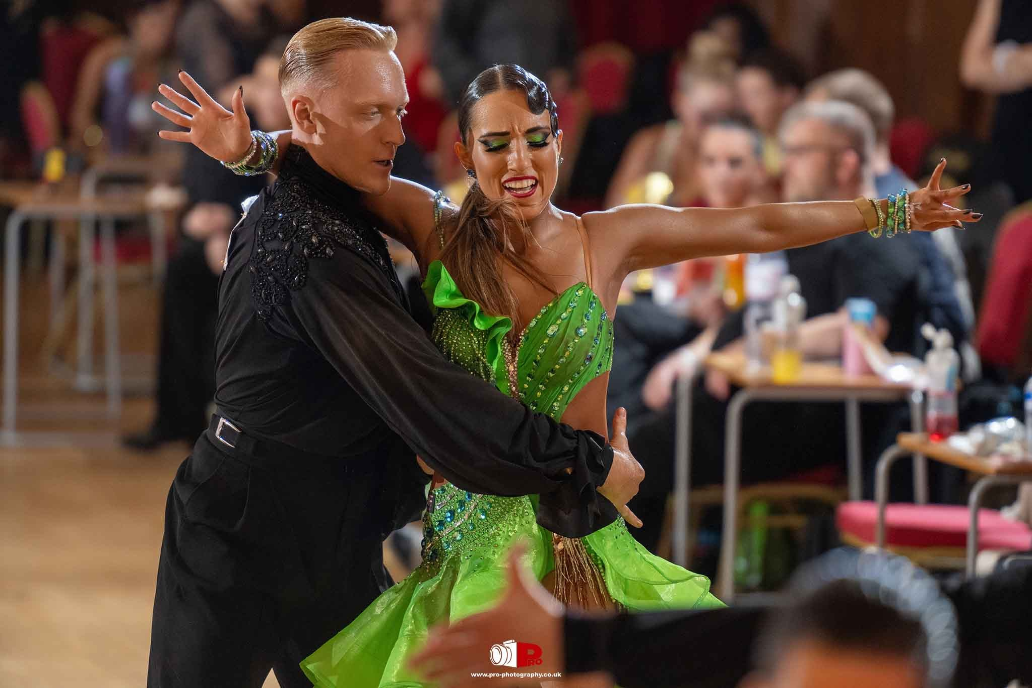 A female dancer in a dazzling green dress dances energetically with her partner in a lively Latin performance.