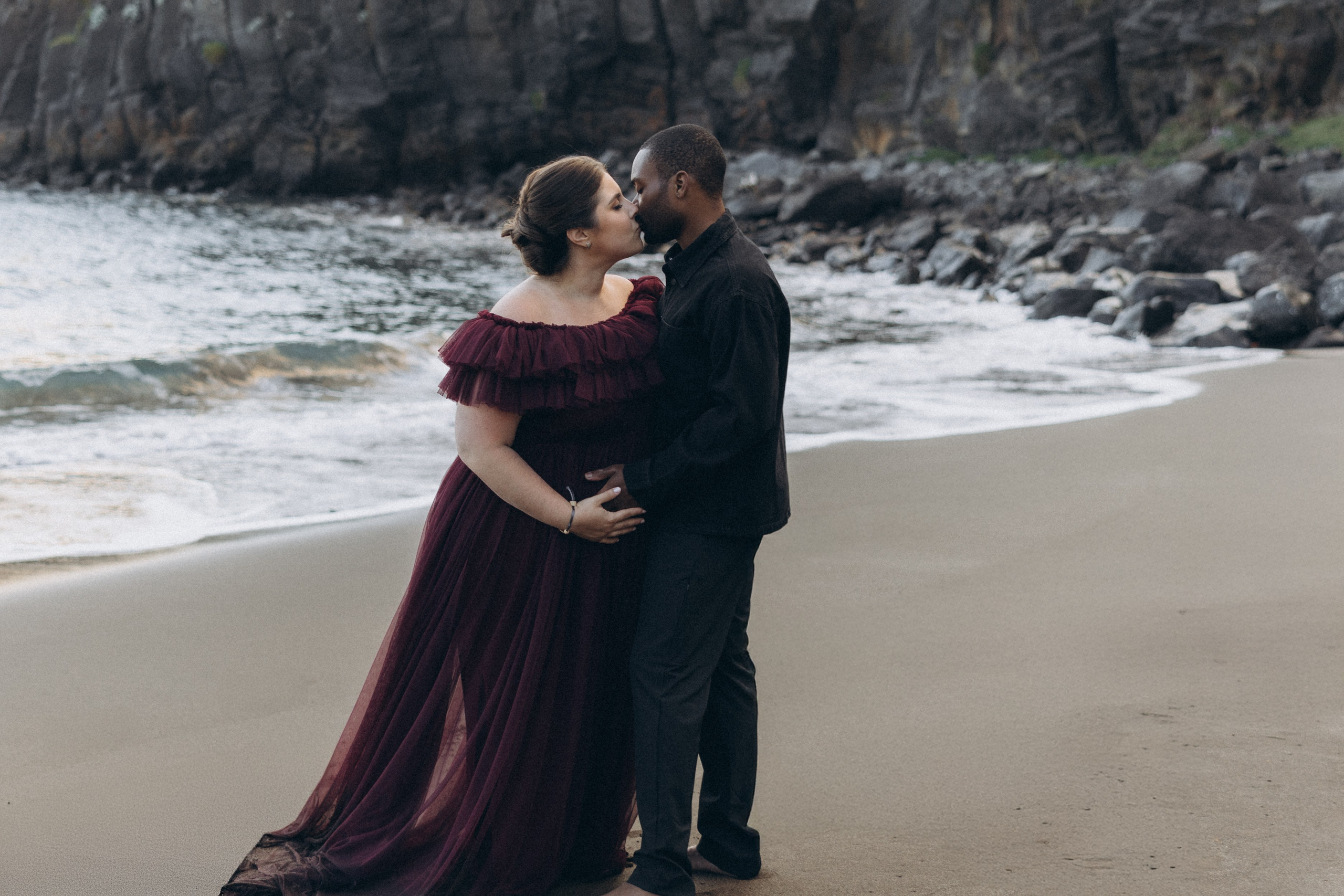 A glowing expectant mother standing on a cliff overlooking the ocean in Madeira, her dress flowing gently in the wind as the golden sunset casts a warm glow.