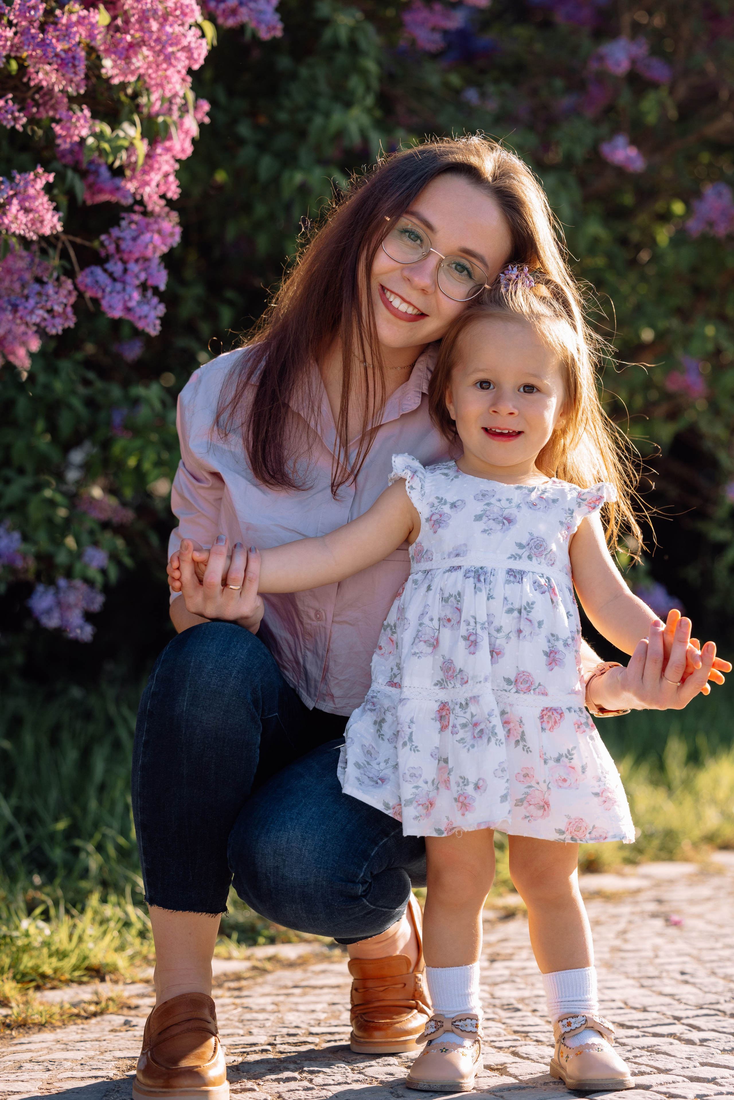 Mama und Tochter lachen zusammen zwischen blühendem Flieder am Schloss Nymphenburg