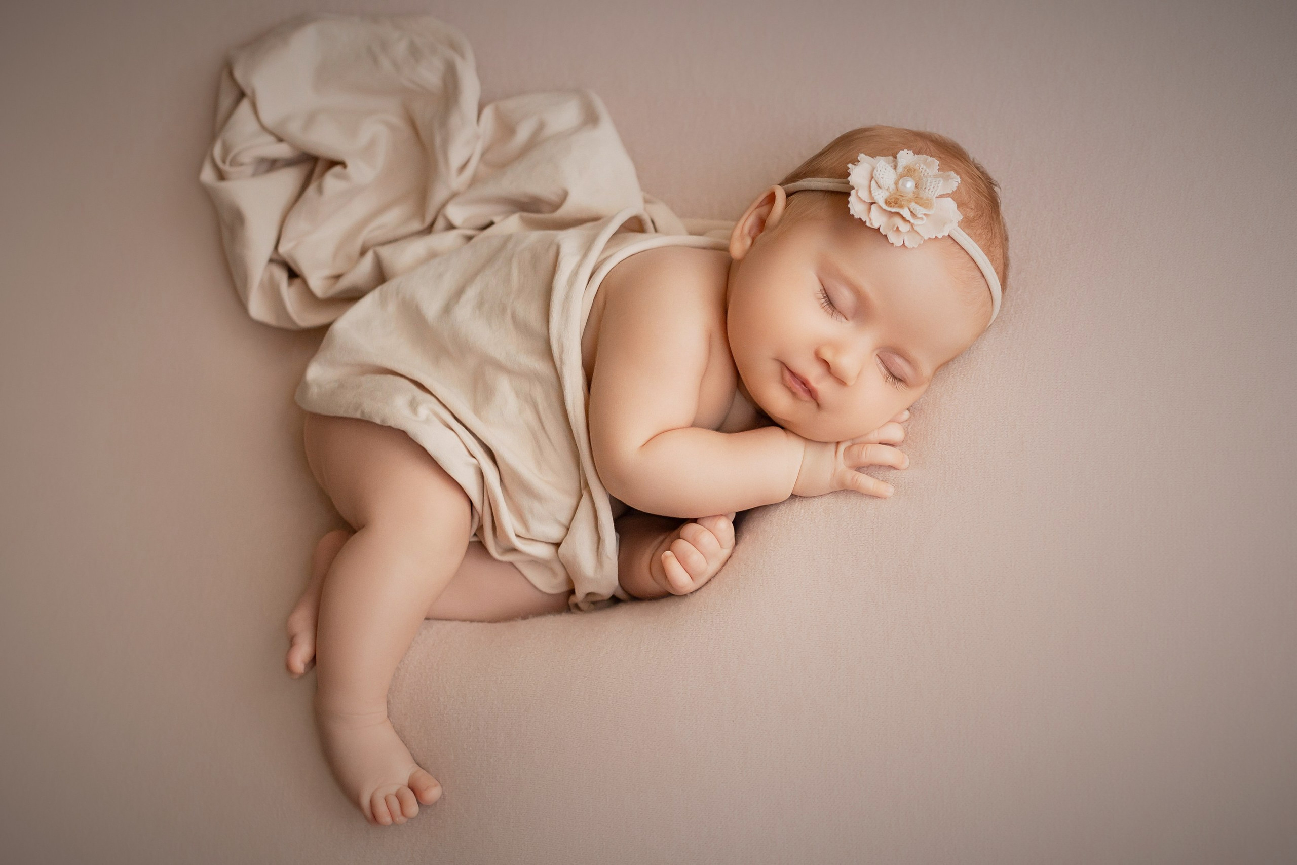 Newborn baby girl sleeping under a blanket with floral headband