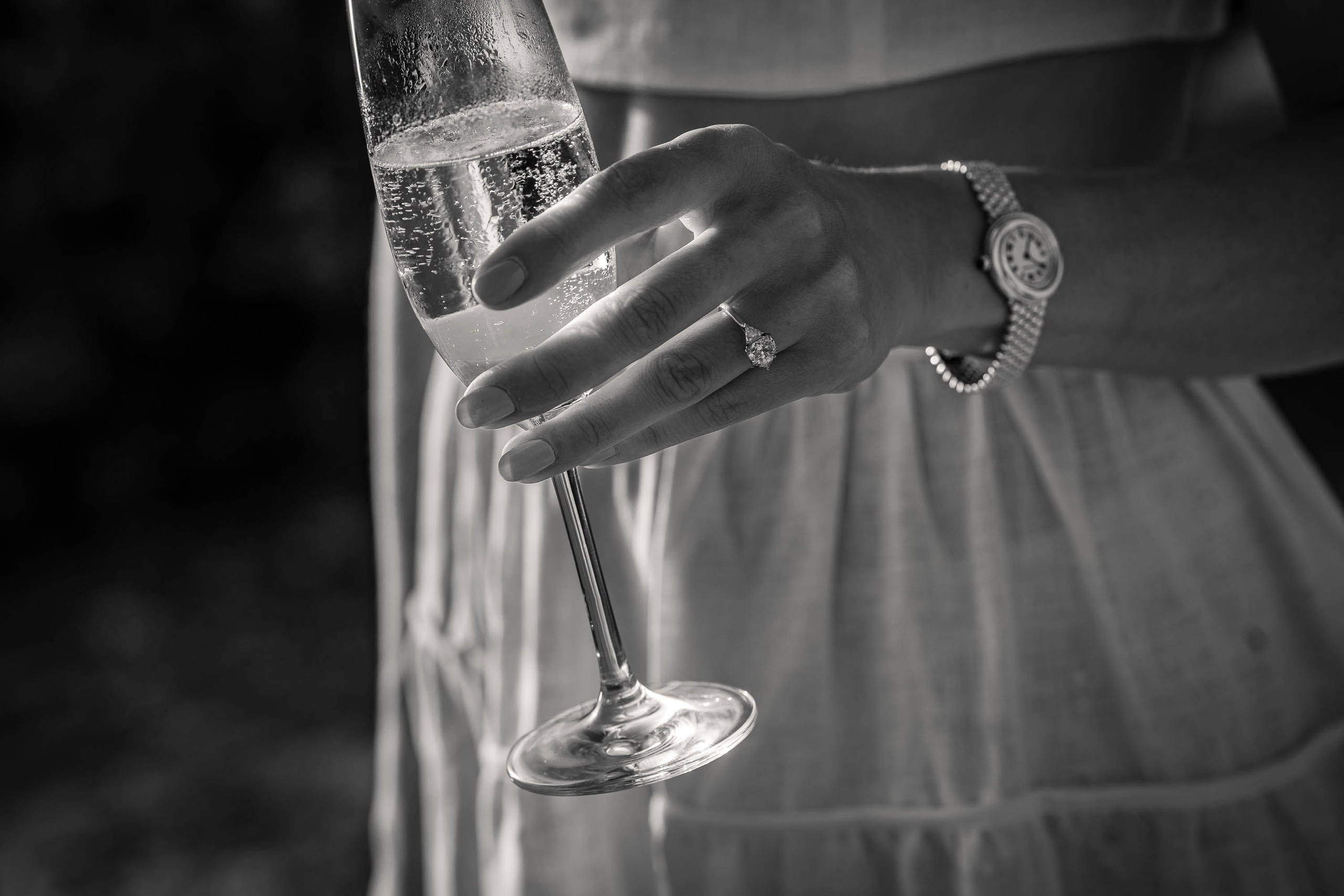 Her engaged ring on her finger, a glass of champagne in her hand at sunset at Cap Rocat venue