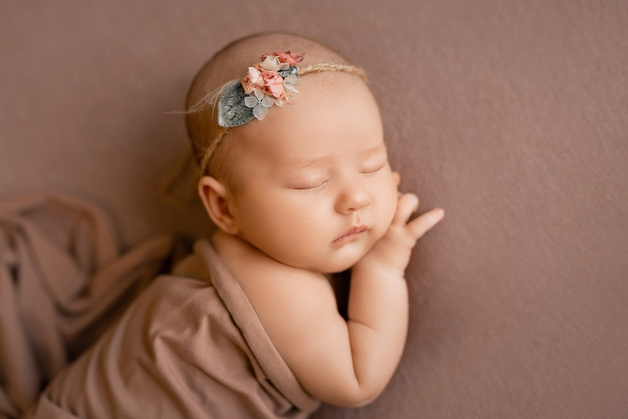 Newborn baby girl sleeping in delicate wrap with headband