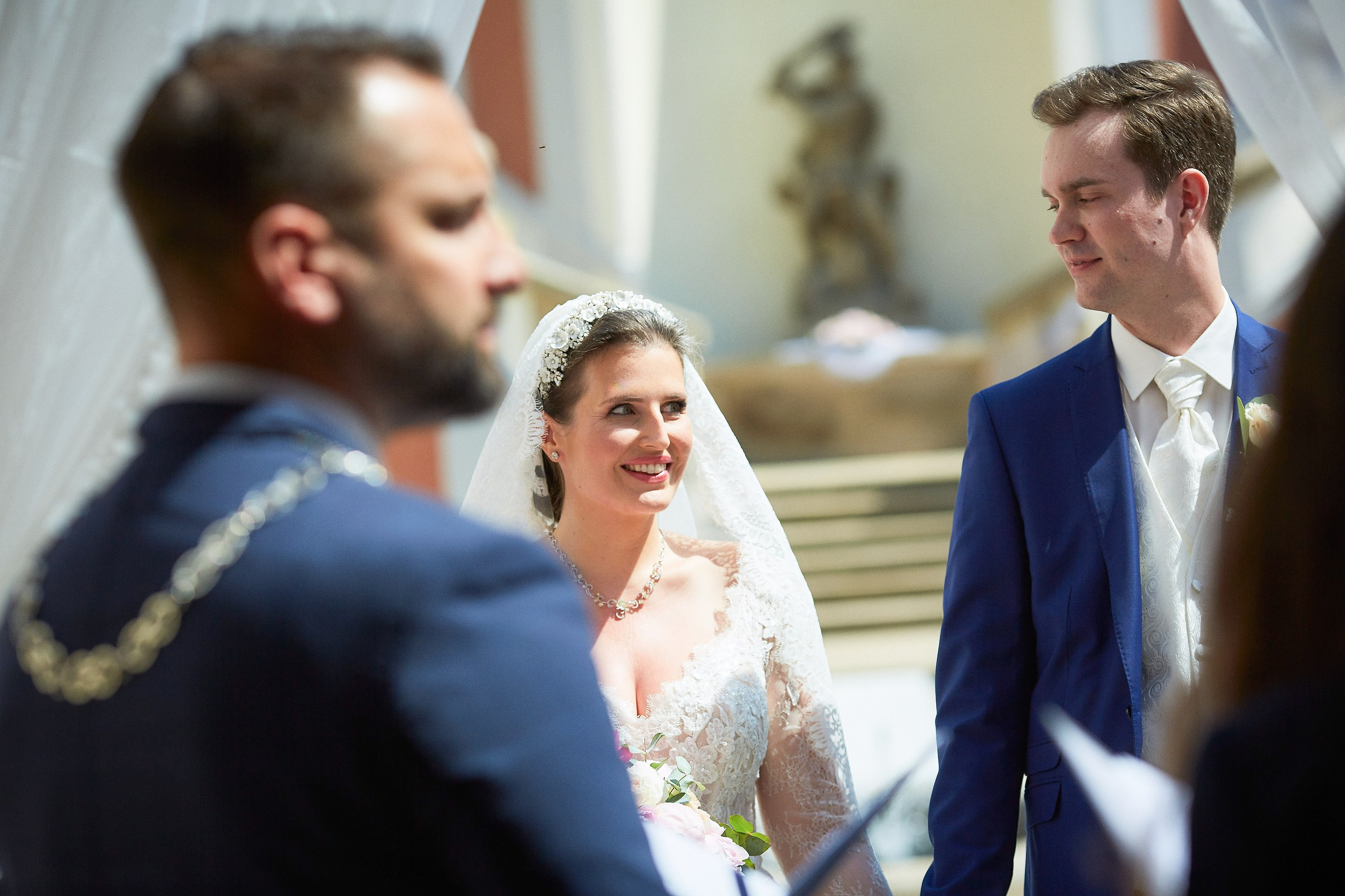The bride and groom sneak a peek at one another as the wedding officiant gives his speech under the floral arch at the Ledebour Garden.