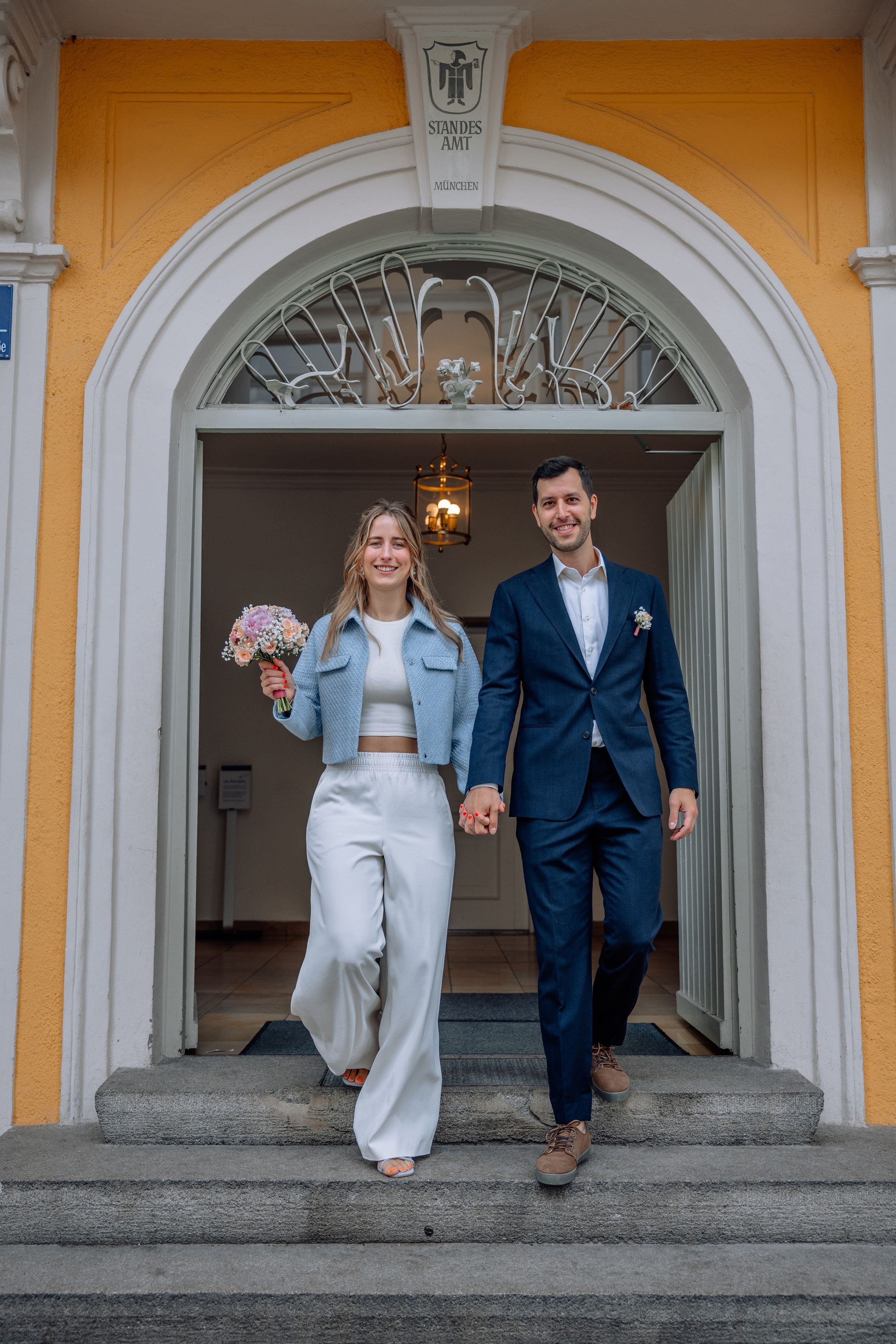 Brautpaar läuft Treppe des Standesamts Schwabing hinunter – Gäste im Hintergrund