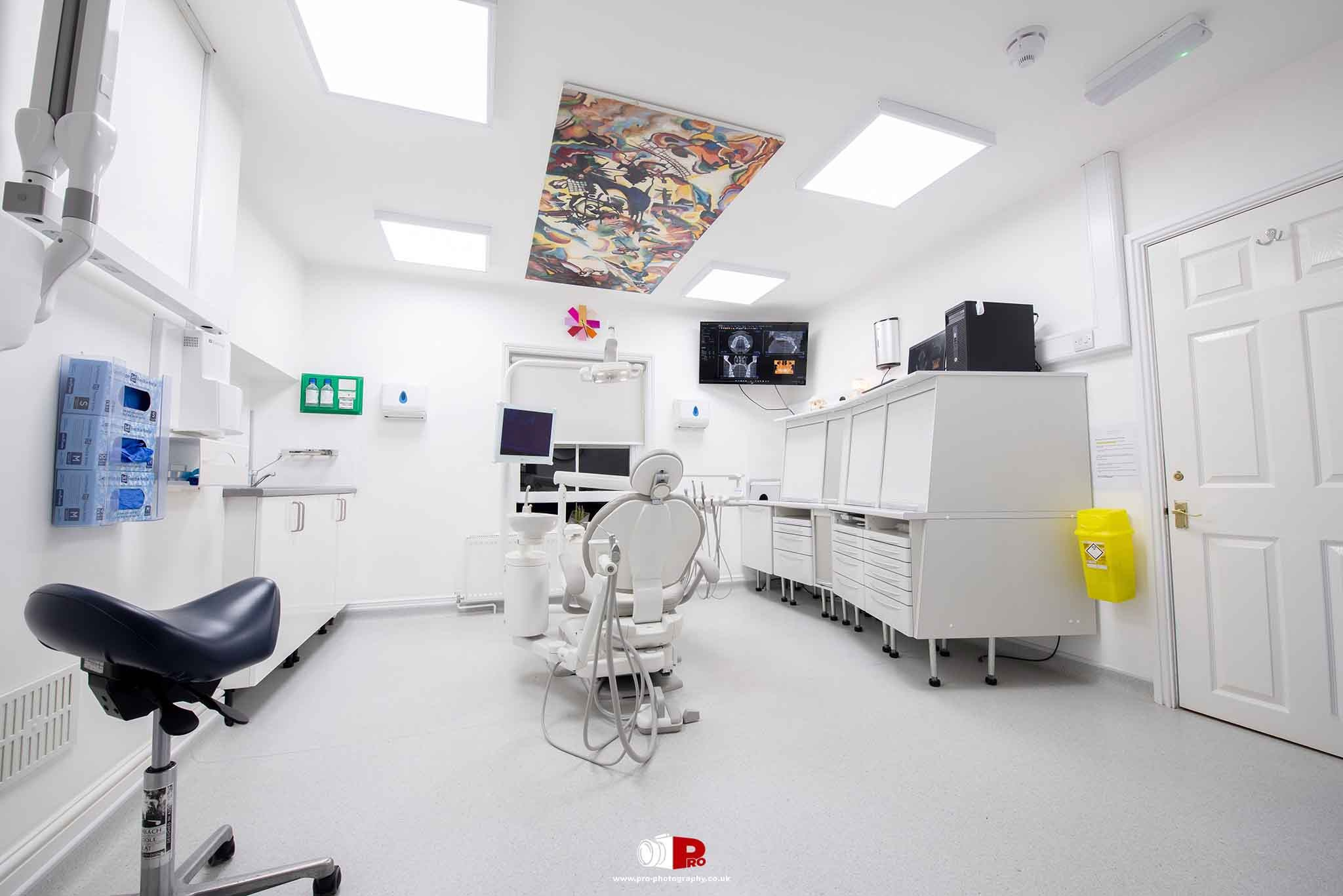 Bright dental clinic interior with white furnishings, ceiling art, and advanced dental equipment.