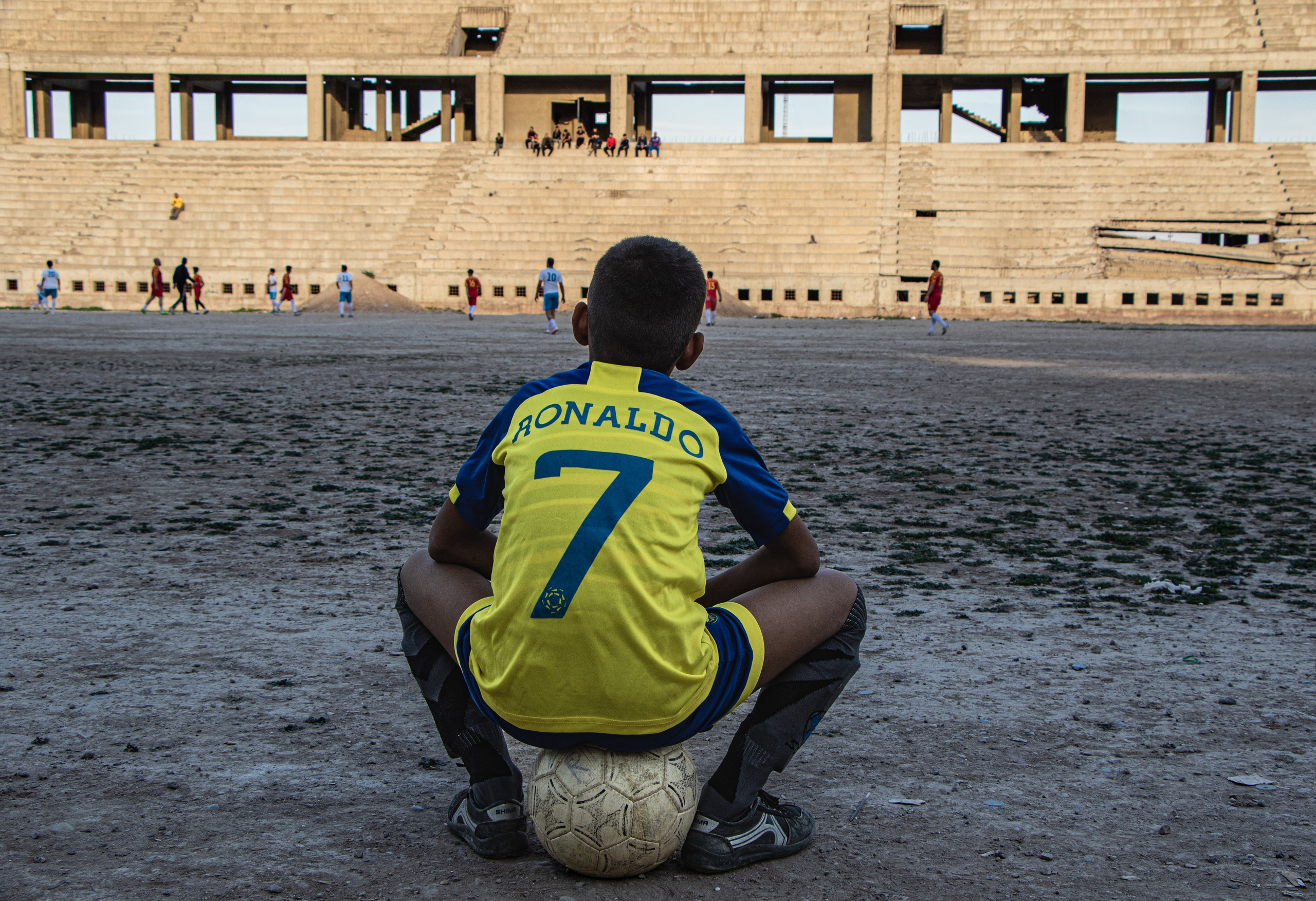 Un jeune Irakien assis sur son ballon dans le stade de Mossoul, désormais en ruines.