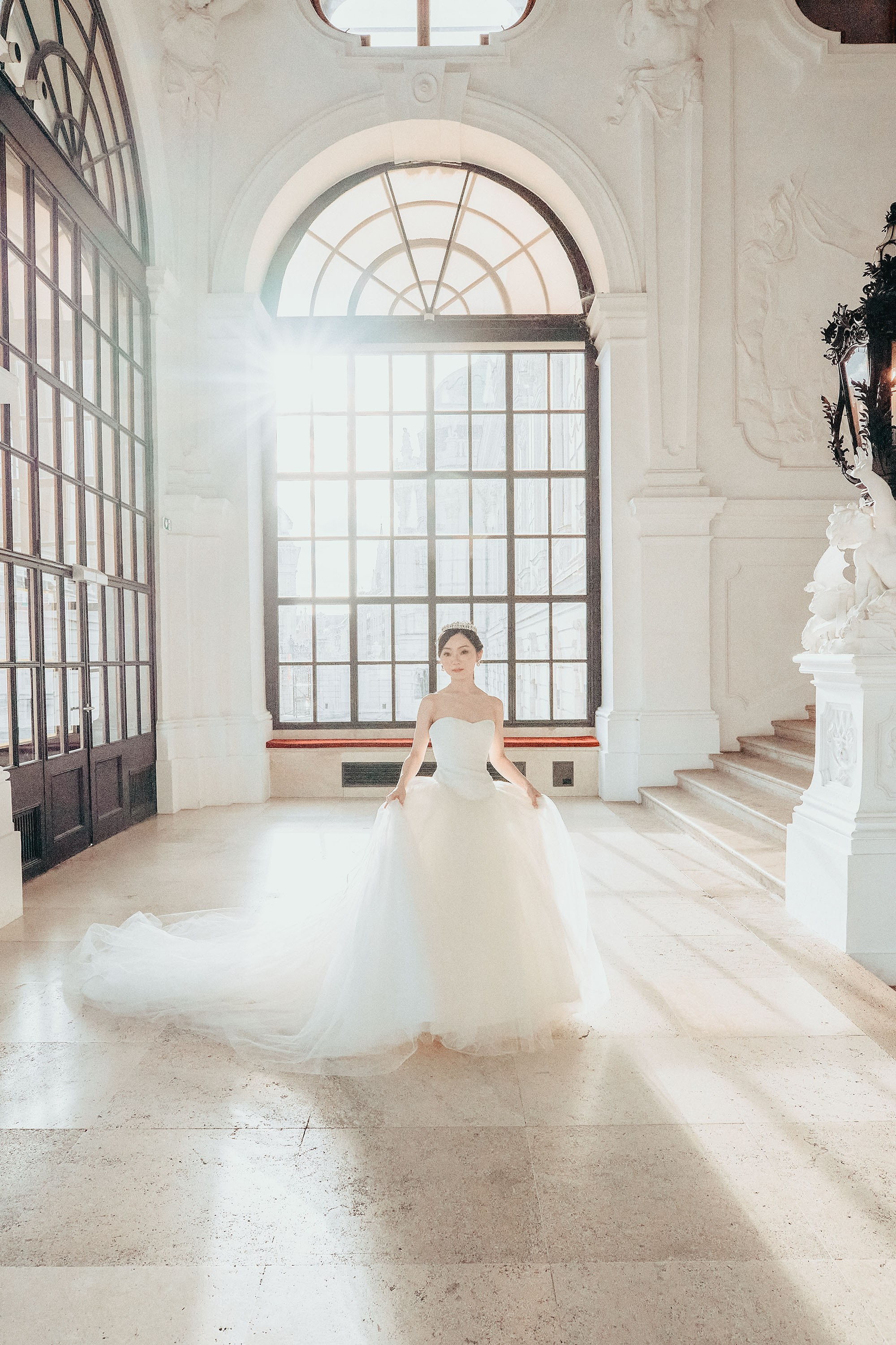 As the sun flares vividly around her, a bride stands in the middle of the oppulent Grand Staircase at the Belvedere Palace.