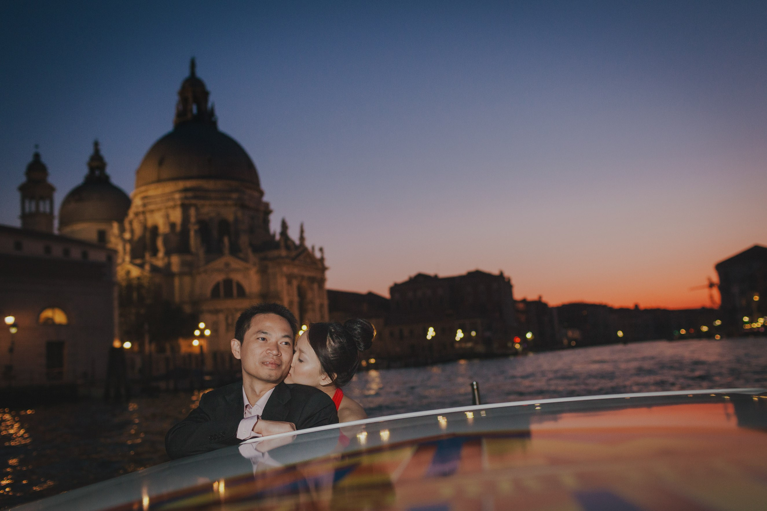 A Thai couple snuggle up as the sky flares dramatically aboard their private tour of Venice aboard a boat.