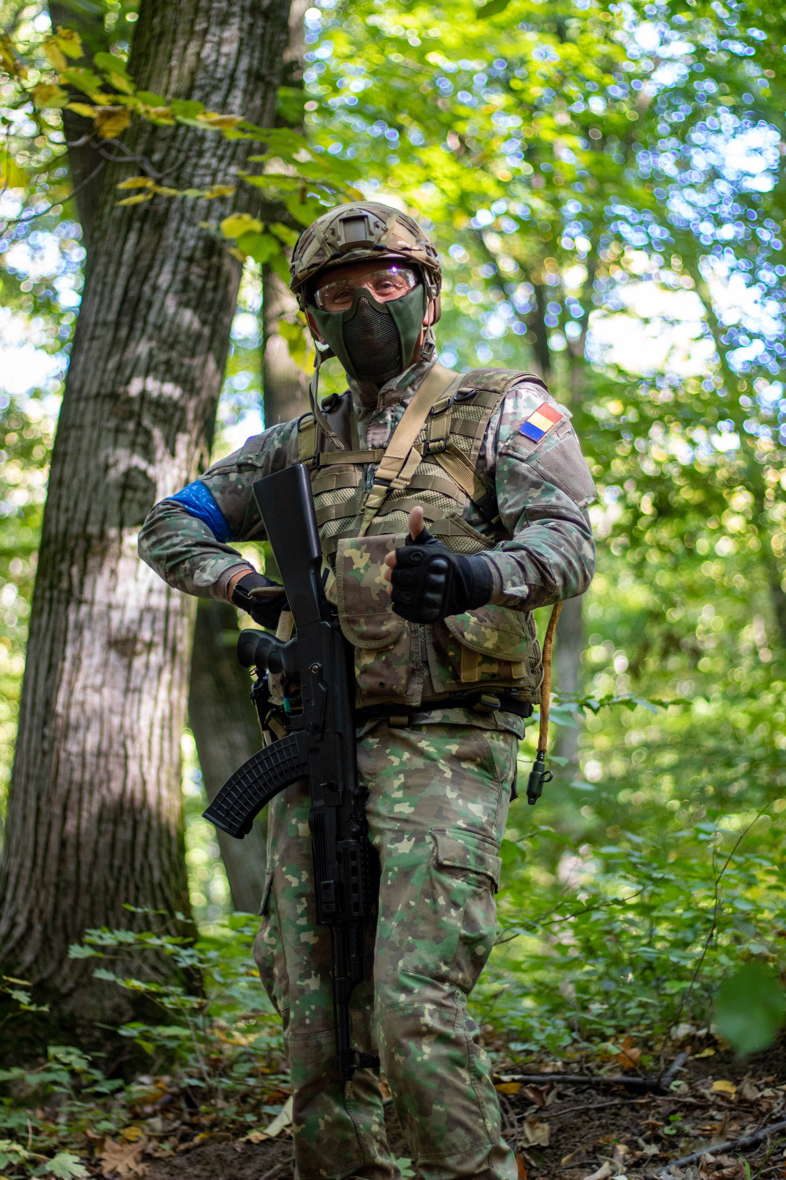 Person leaning against a tree in a green forest, blending with nature and wearing outdoor gear.