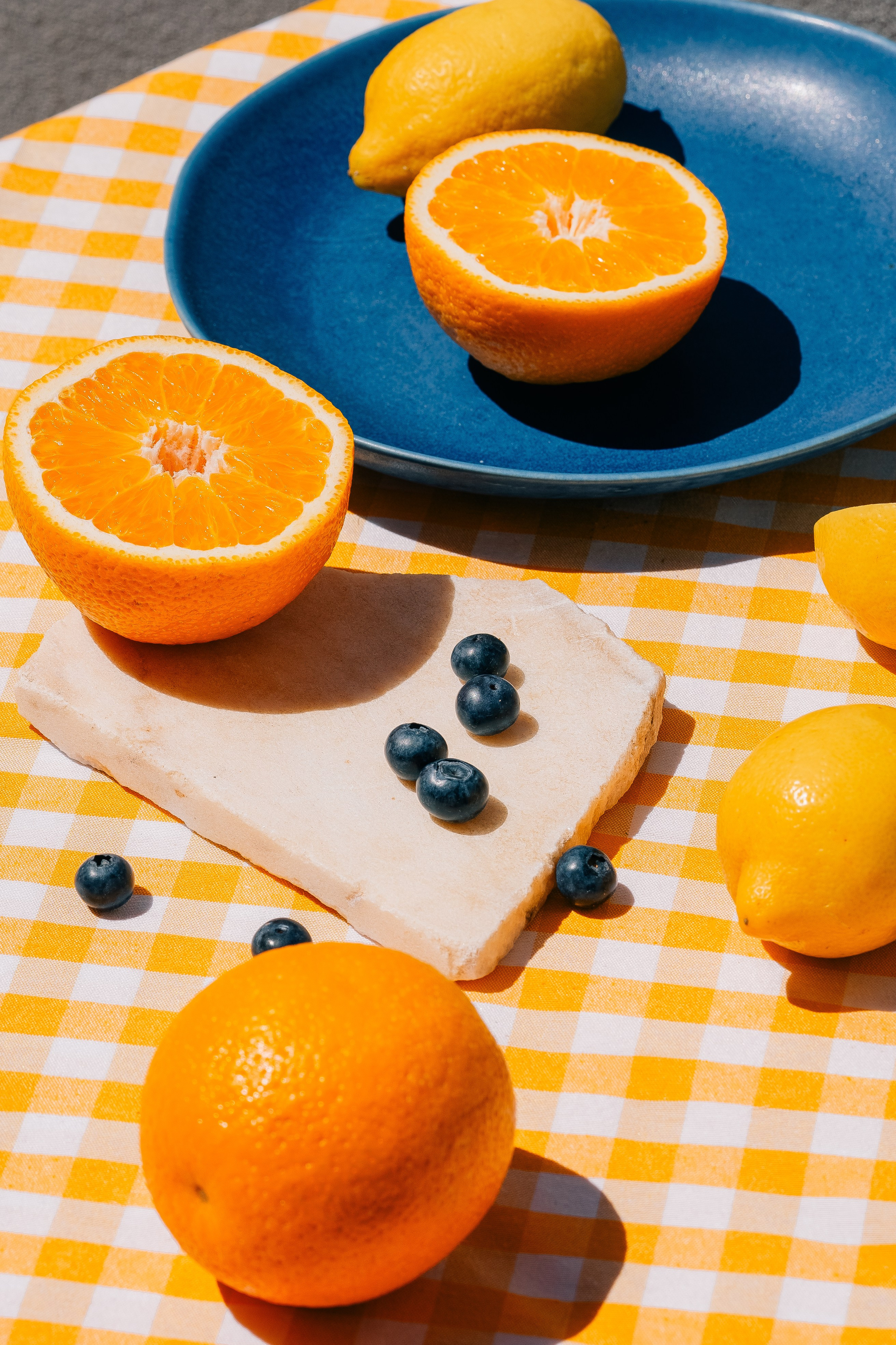 Citrinos frescos e mirtilos na toalha de mesa quadriculada. Frutas cítricas brilhantes e mirtilos dispostos em uma toalha amarela branca quadriculada na luz do sol.