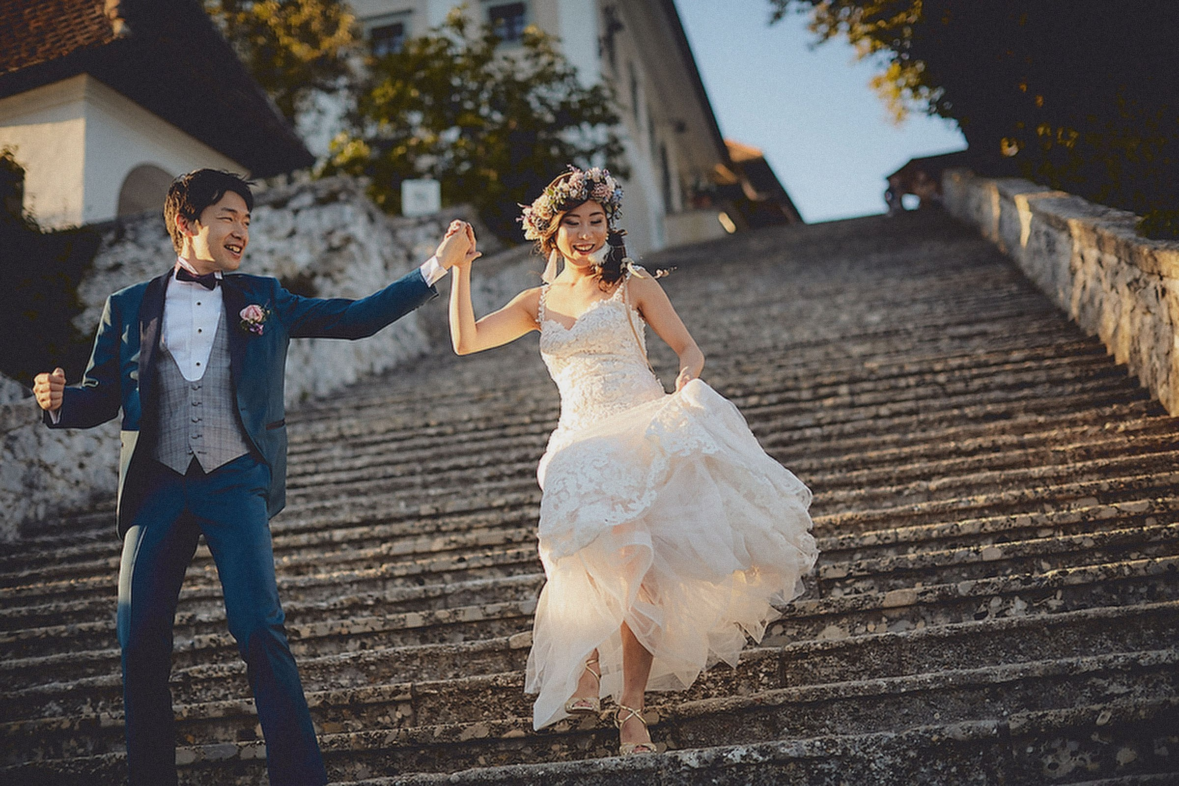 A happy Japanese bride and groom hold their hands high in the air as they descend 99 steps on the historic Bled Island.