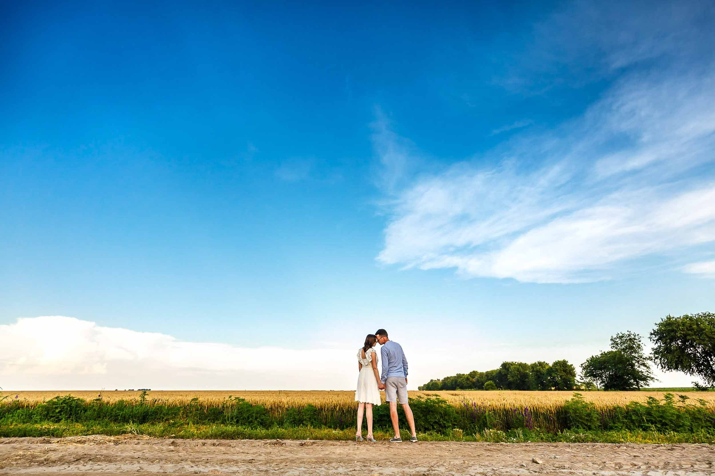 Romantični mladenci šetaju stazom okruženom prirodom, pod vedrim plavim nebom
