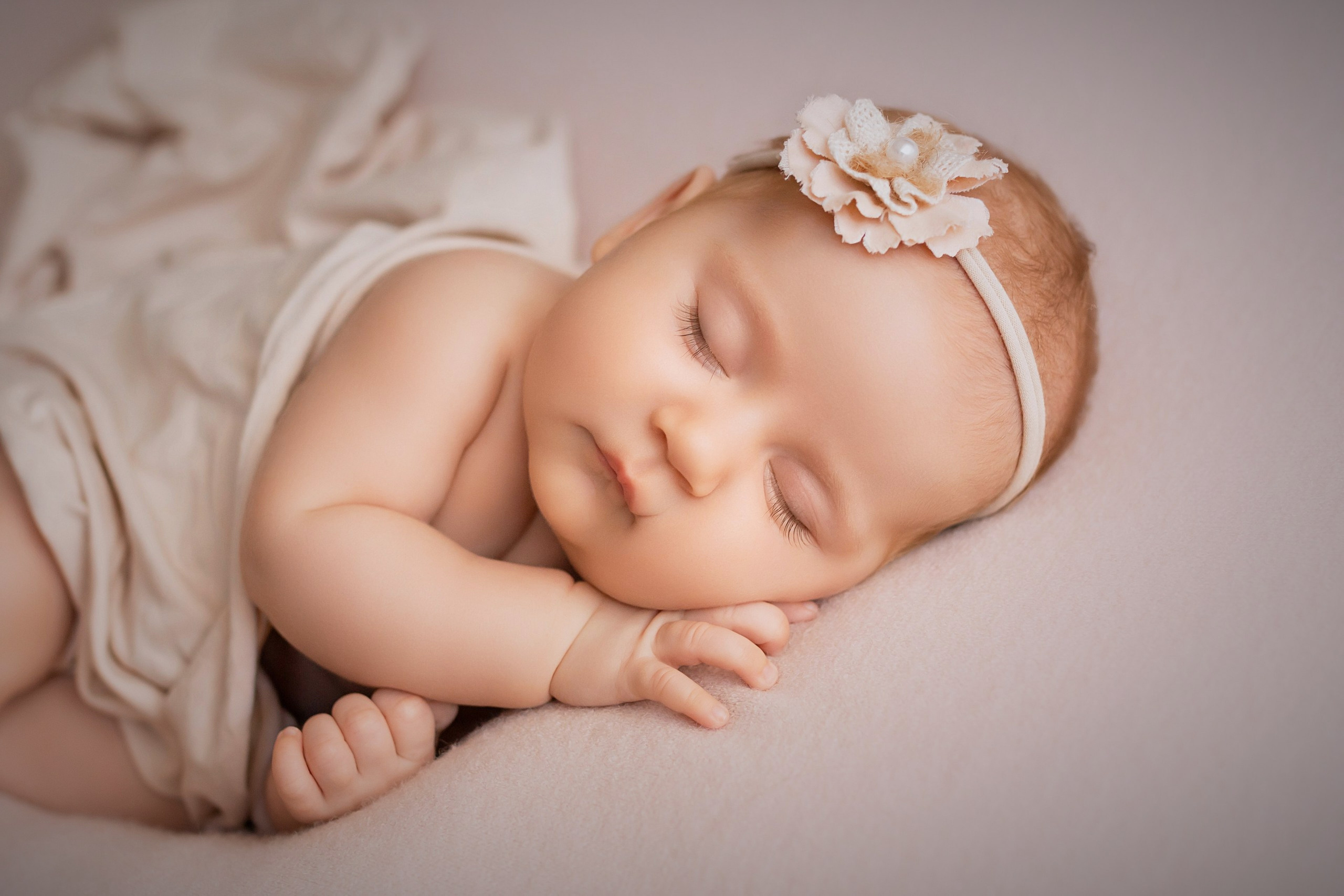 Sleeping newborn girl in elegant headband on neutral backdrop