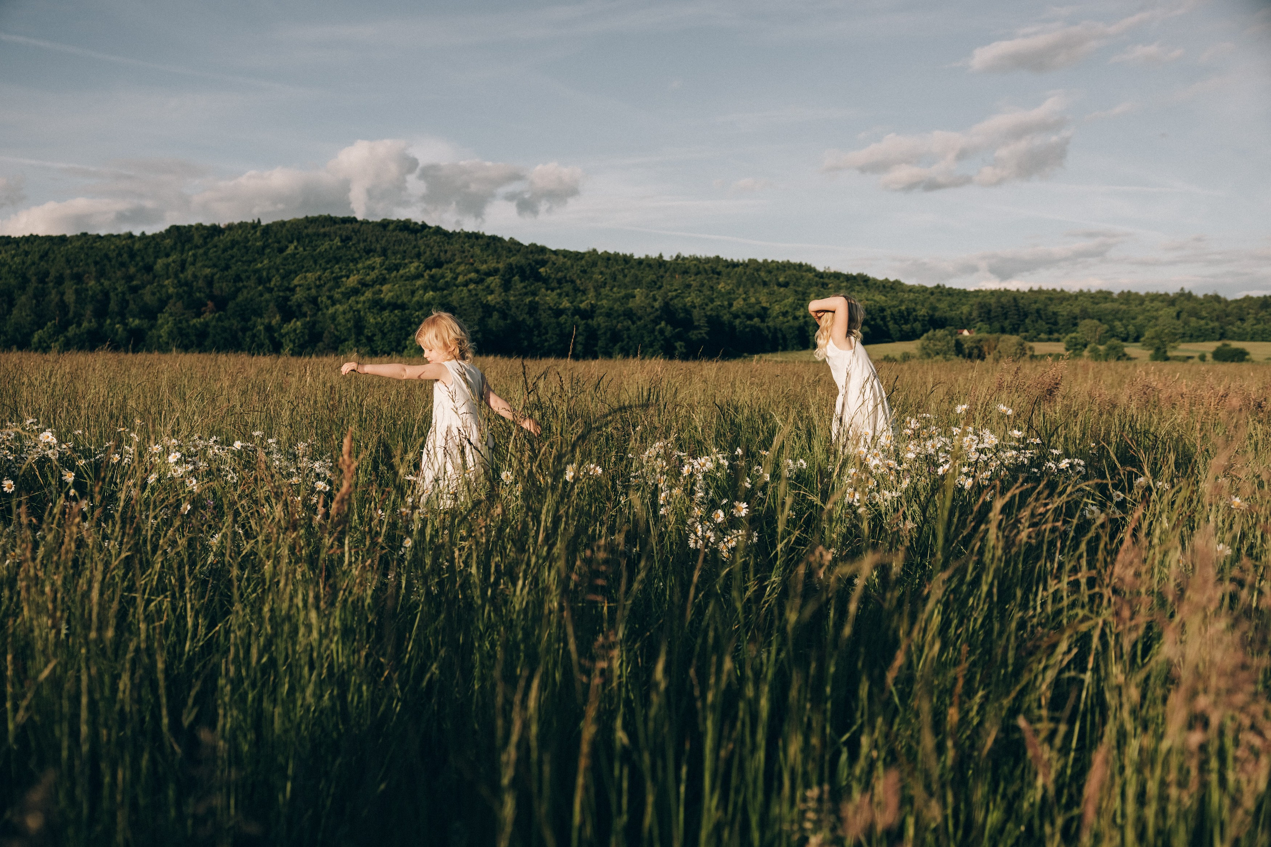 Family photoshoot in a daisy meadow at golden hour — natural light, warm tones, candid moments between a mother and her daughters. Lifestyle and Family Photographer in Pisek Oxana Telupilova