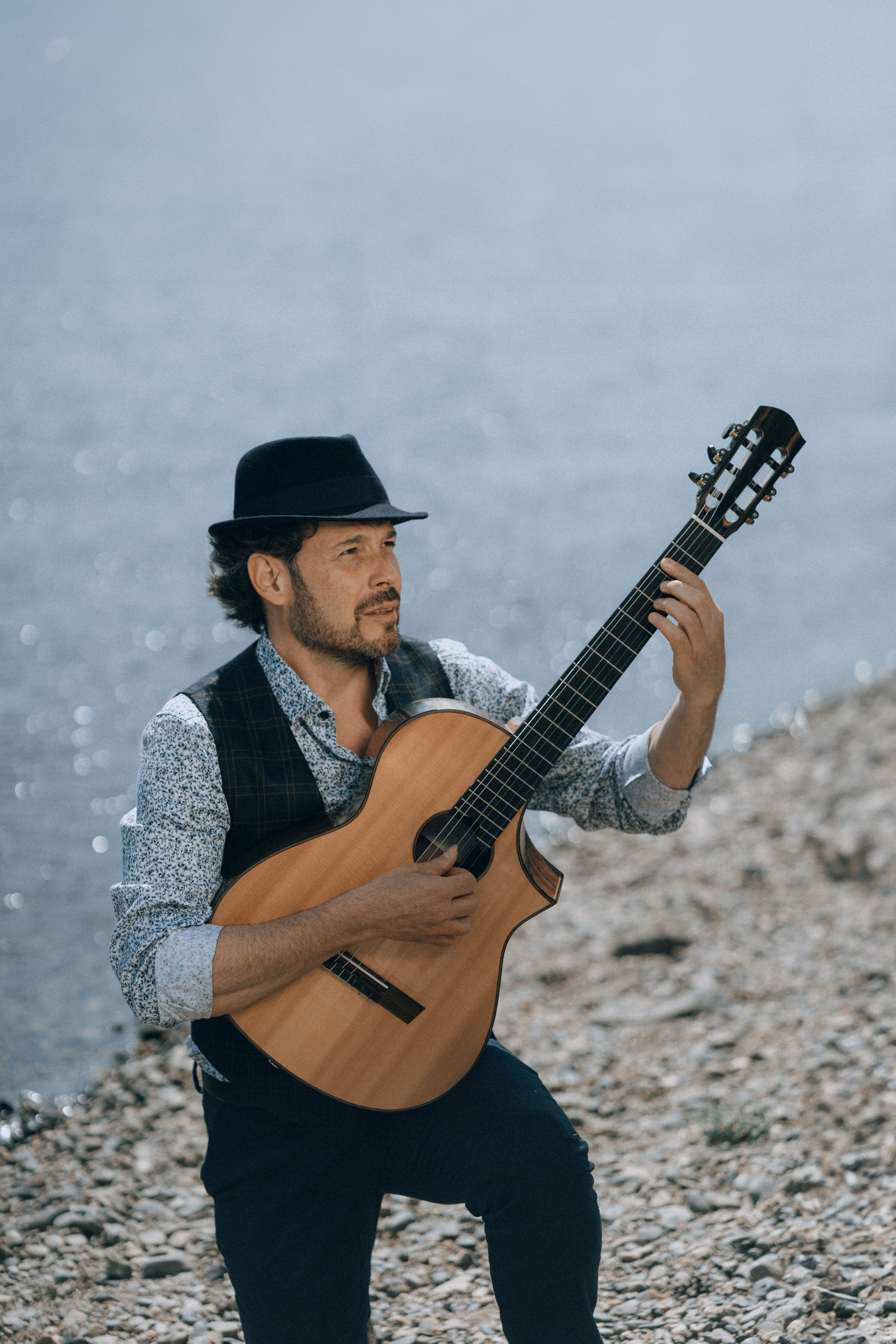 Gitarrist mit Hut sitzt am Flussufer und spielt