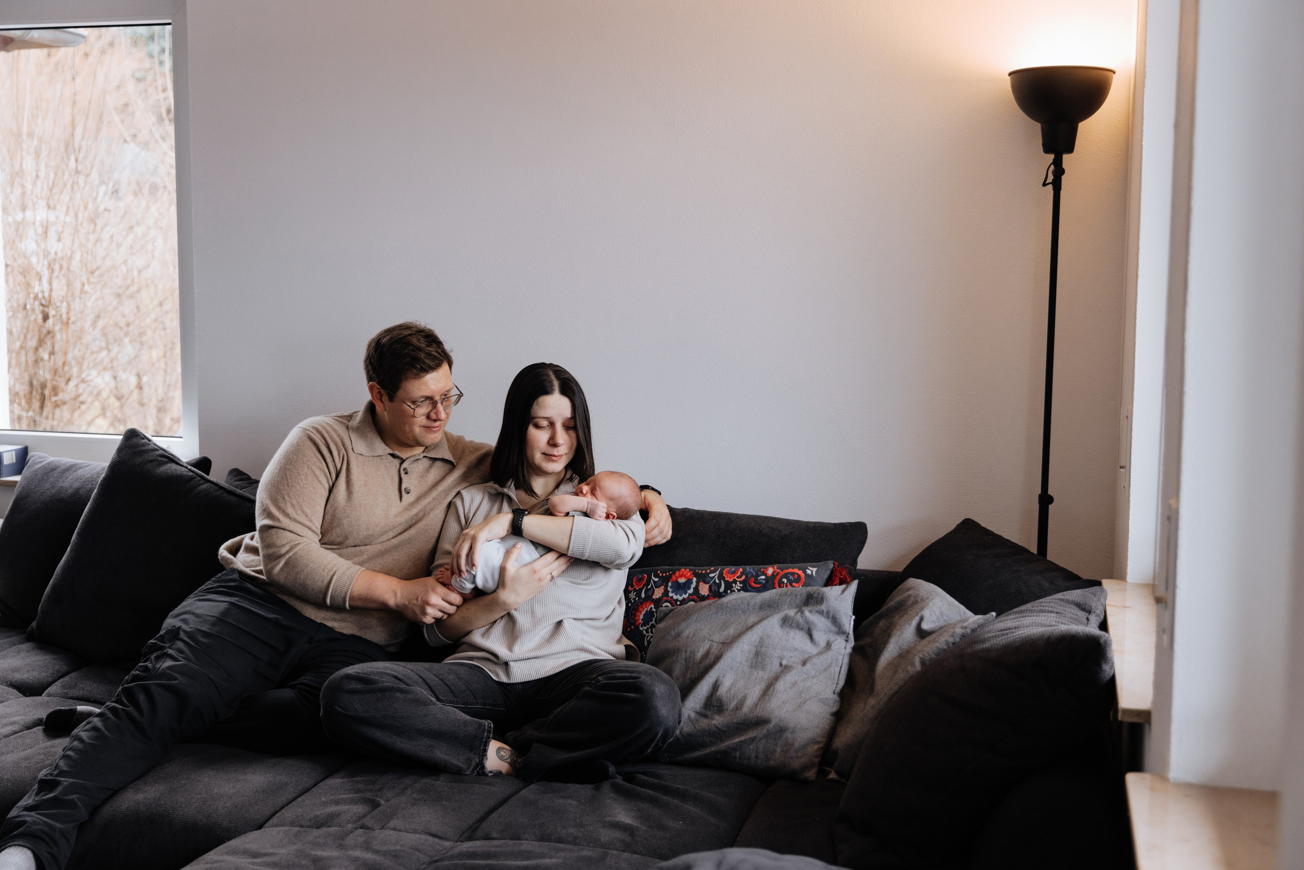 Eltern sitzen mit ihrem Baby auf dem Sofa zu Hause während einer Familienshooting. Ein gemütlicher und liebevoller Moment.