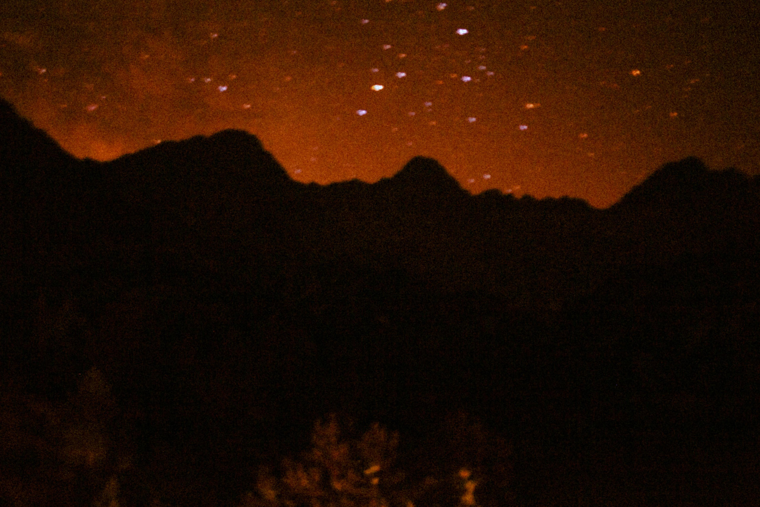 A silhouette of mountains under a starry orange-tinted sky