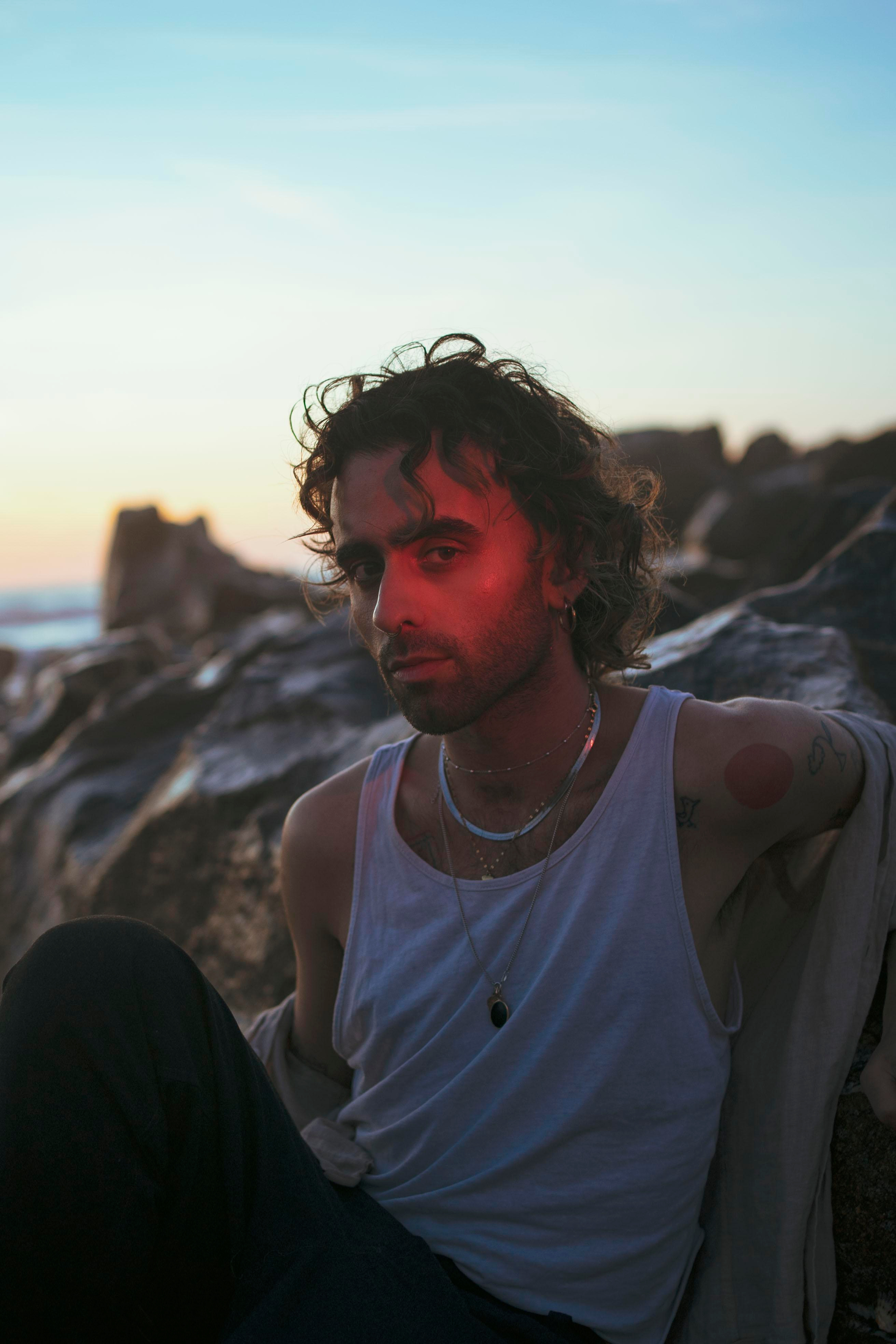 LGBTQ+, LGBT portrait of a beautiful person with makeup, a white tank top, and curly hair. Sunset on a beach, colored light.