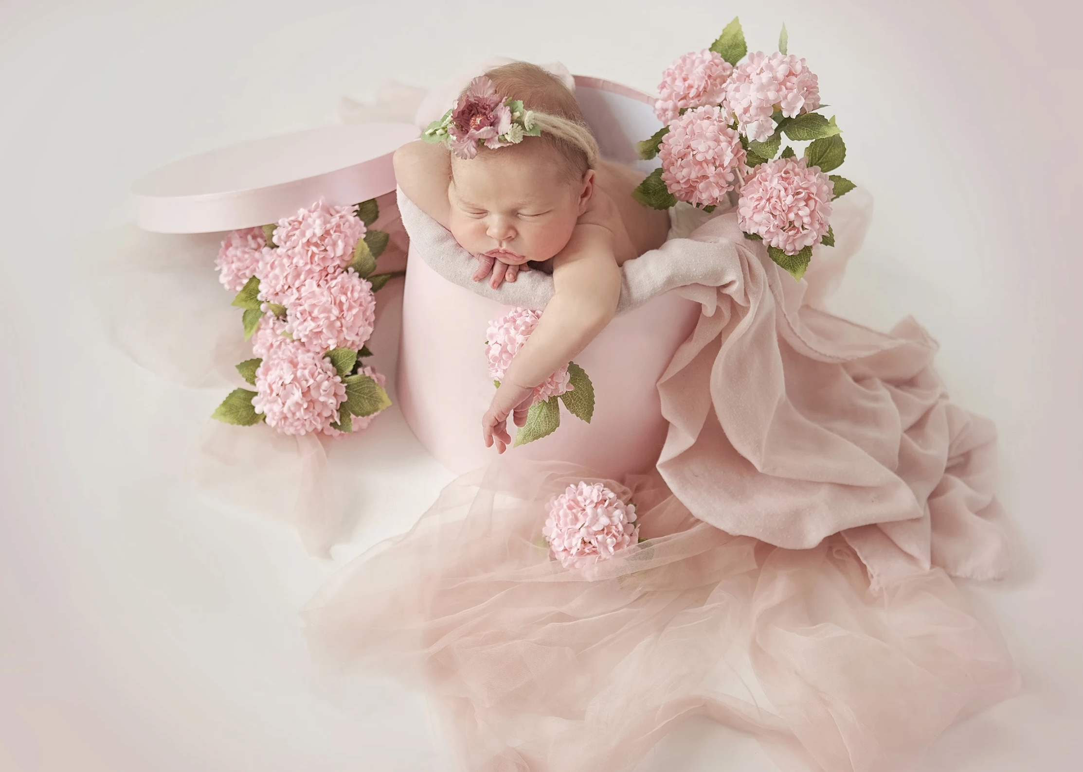 Newborn baby girl sleeping peacefully among soft pink flowers
