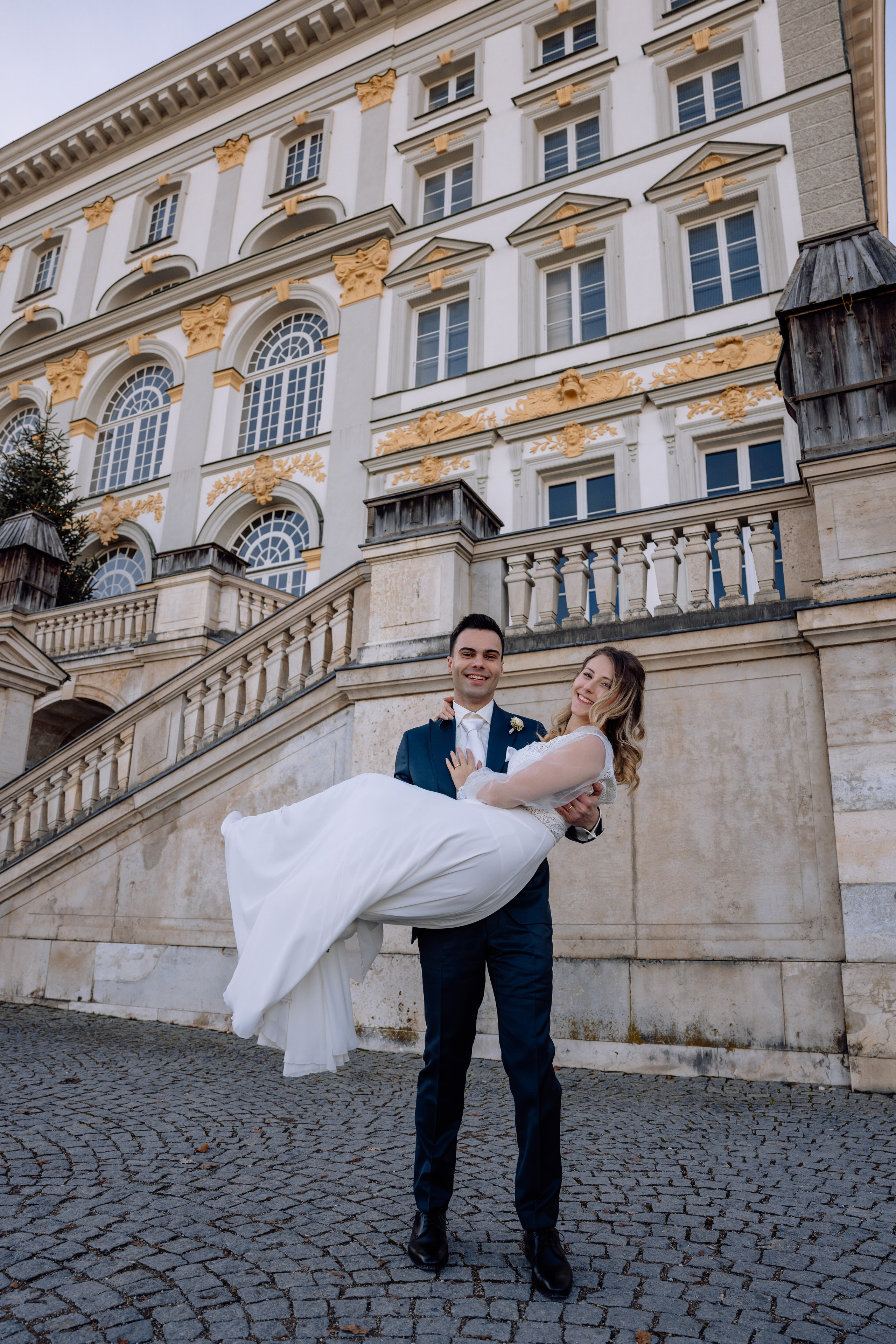 Bräutigam dreht die Braut lachend auf Händen vor dem Schloss Nymphenburg