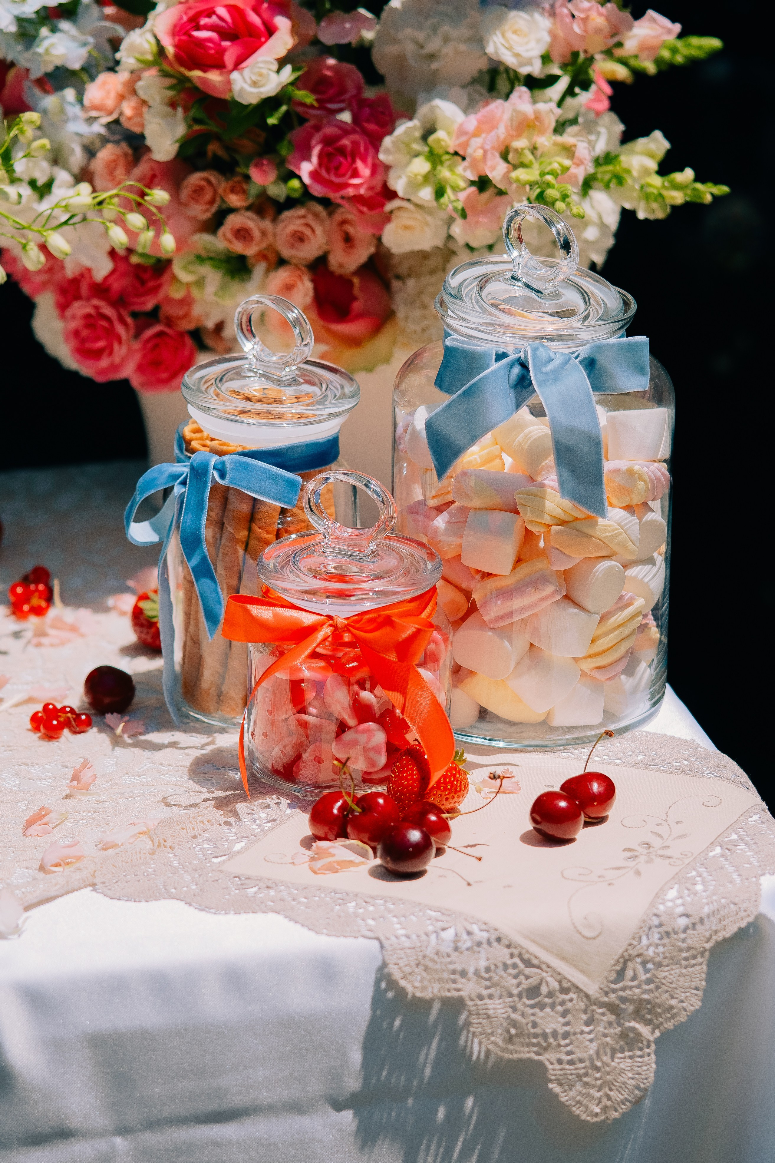 Frascos de vidro com doces e fitas na mesa de sobremesas. Elegantes frascos de vidro cheios de marshmallows e doces, decorados com fitas azuis e vermelhas em uma mesa festiva de sobremesas.