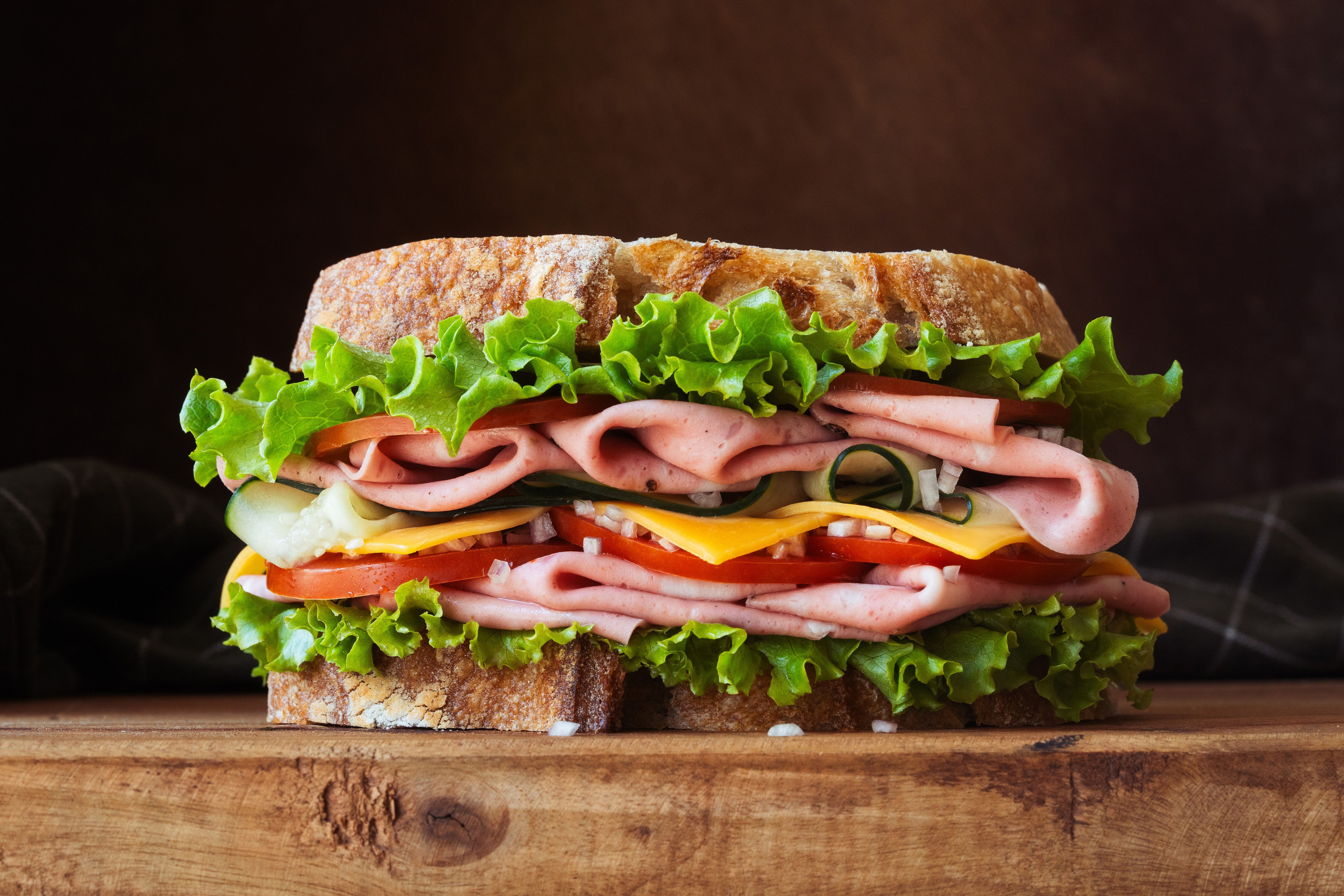 Крупный план большого сэндвича с ветчиной, сыром, салатом, помидорами и огурцами на деревенском хлебе.