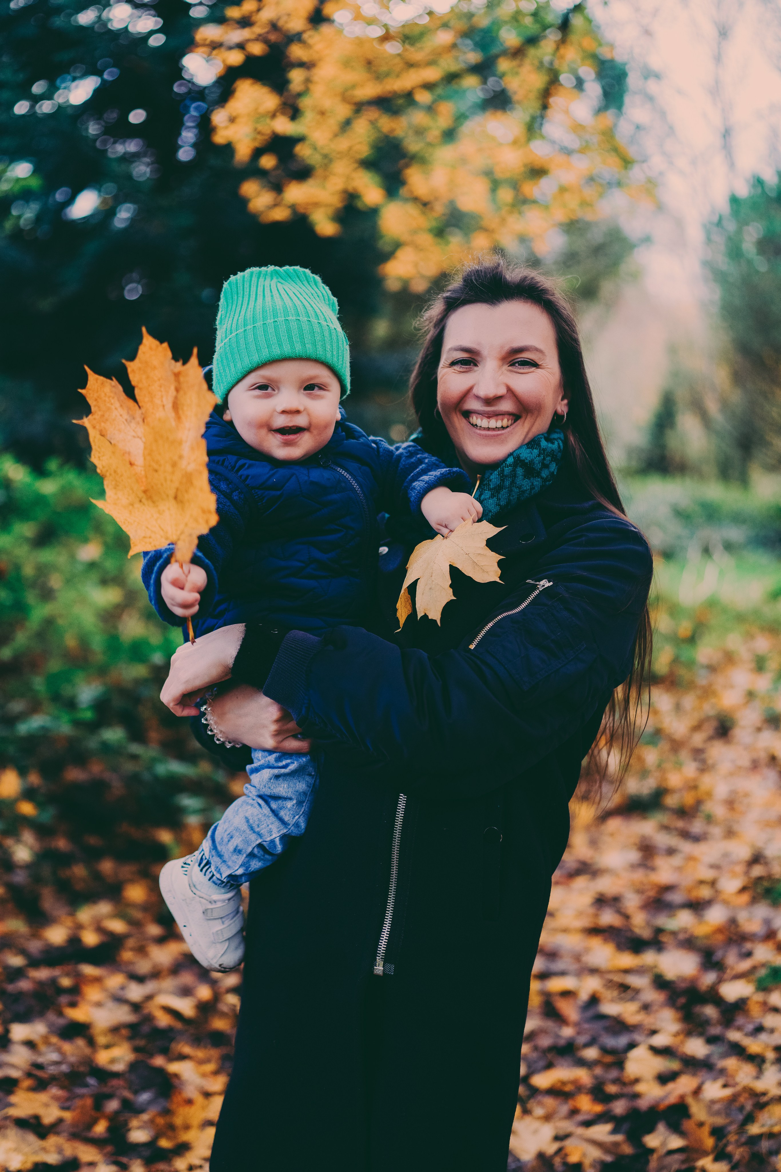 Family photo shoot. Mum is holding toddler with autumn leaf.