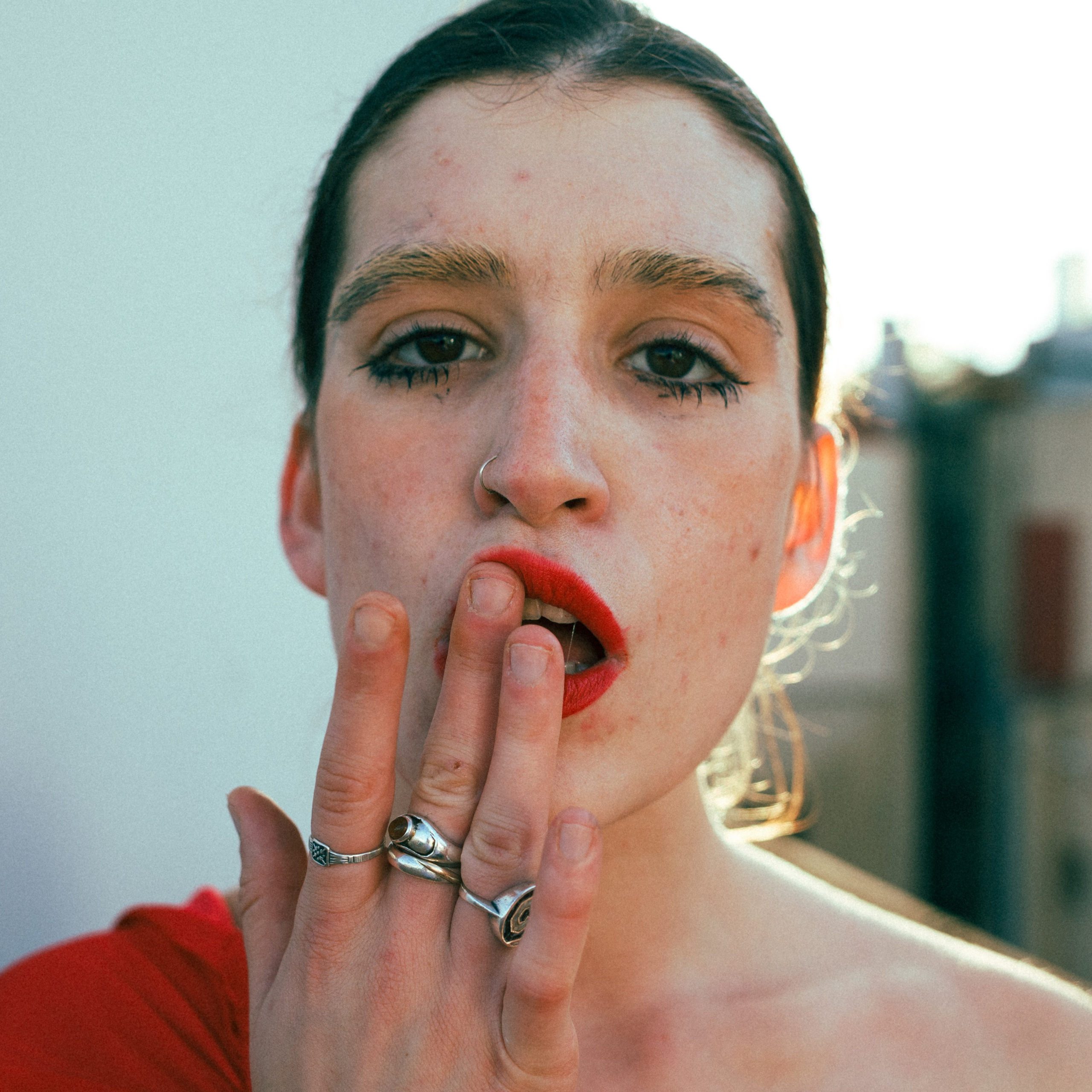 A close-up portrait of a woman with smeared red lipstick, touching her lips