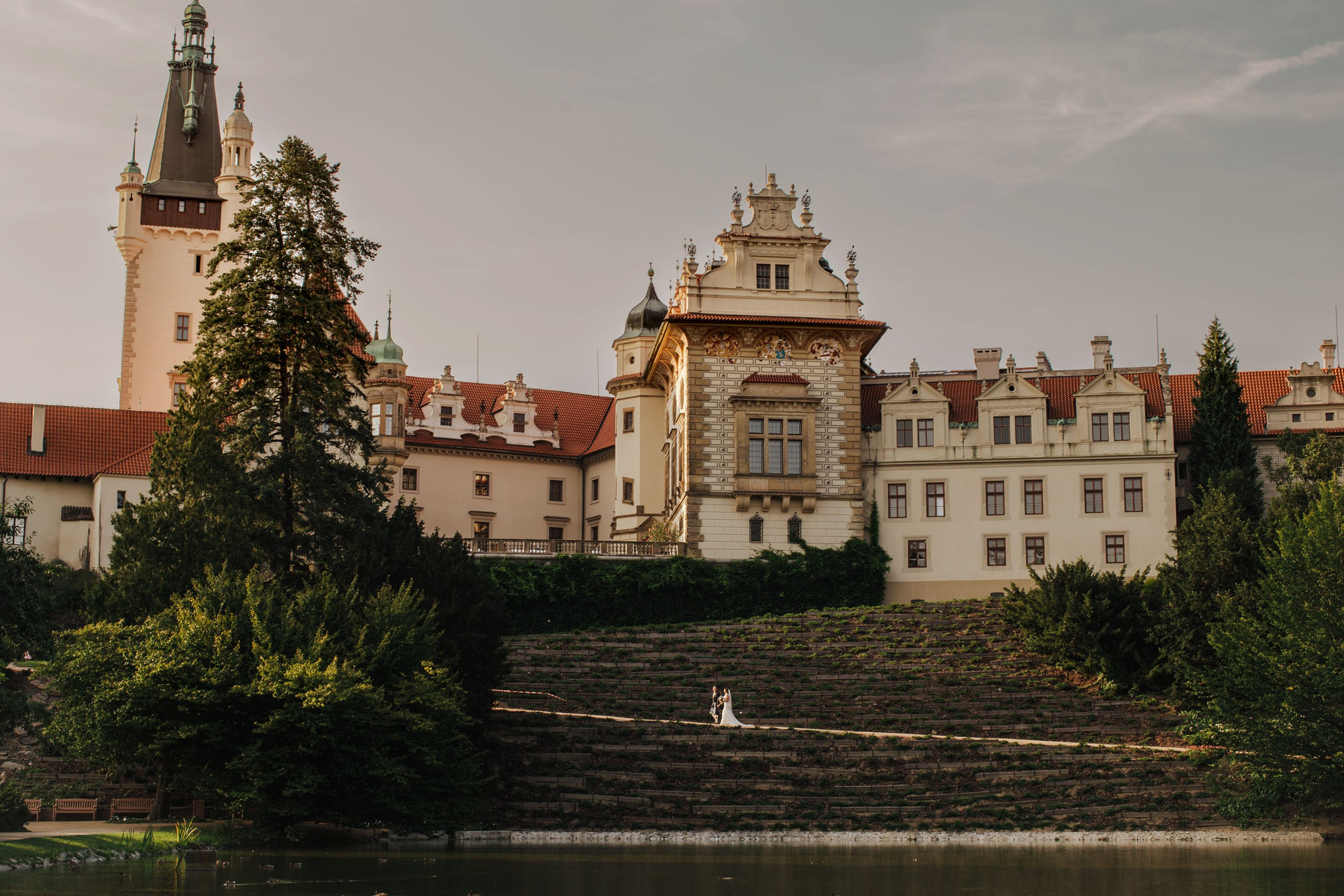 Scottish groom and bride walking into light towards Pruhonice Castle on their wedding day.
