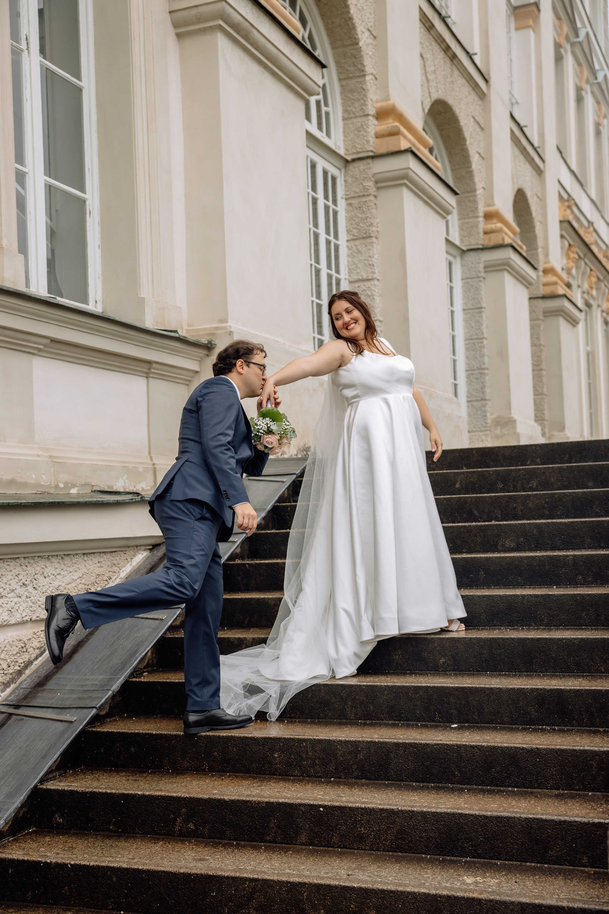 Bräutigam küsst die Hand der Braut beim Spazieren vor dem Schloss Nymphenburg