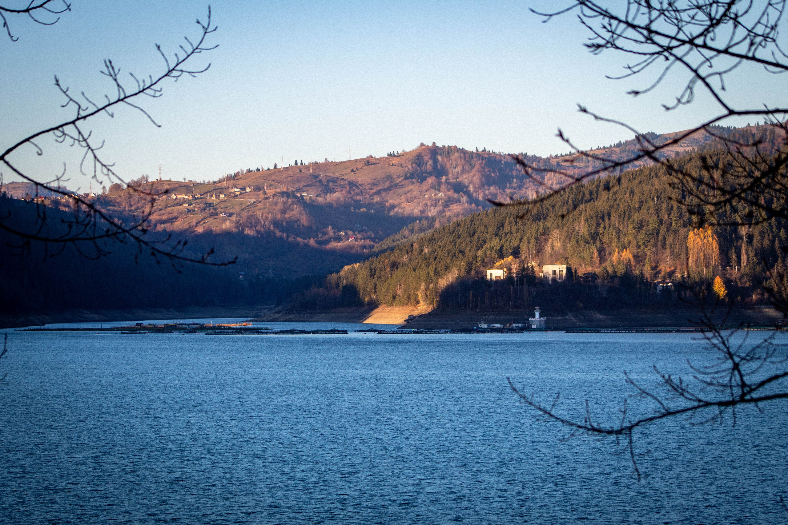 Lake reflecting golden sunset light with hills and trees along the shoreline.