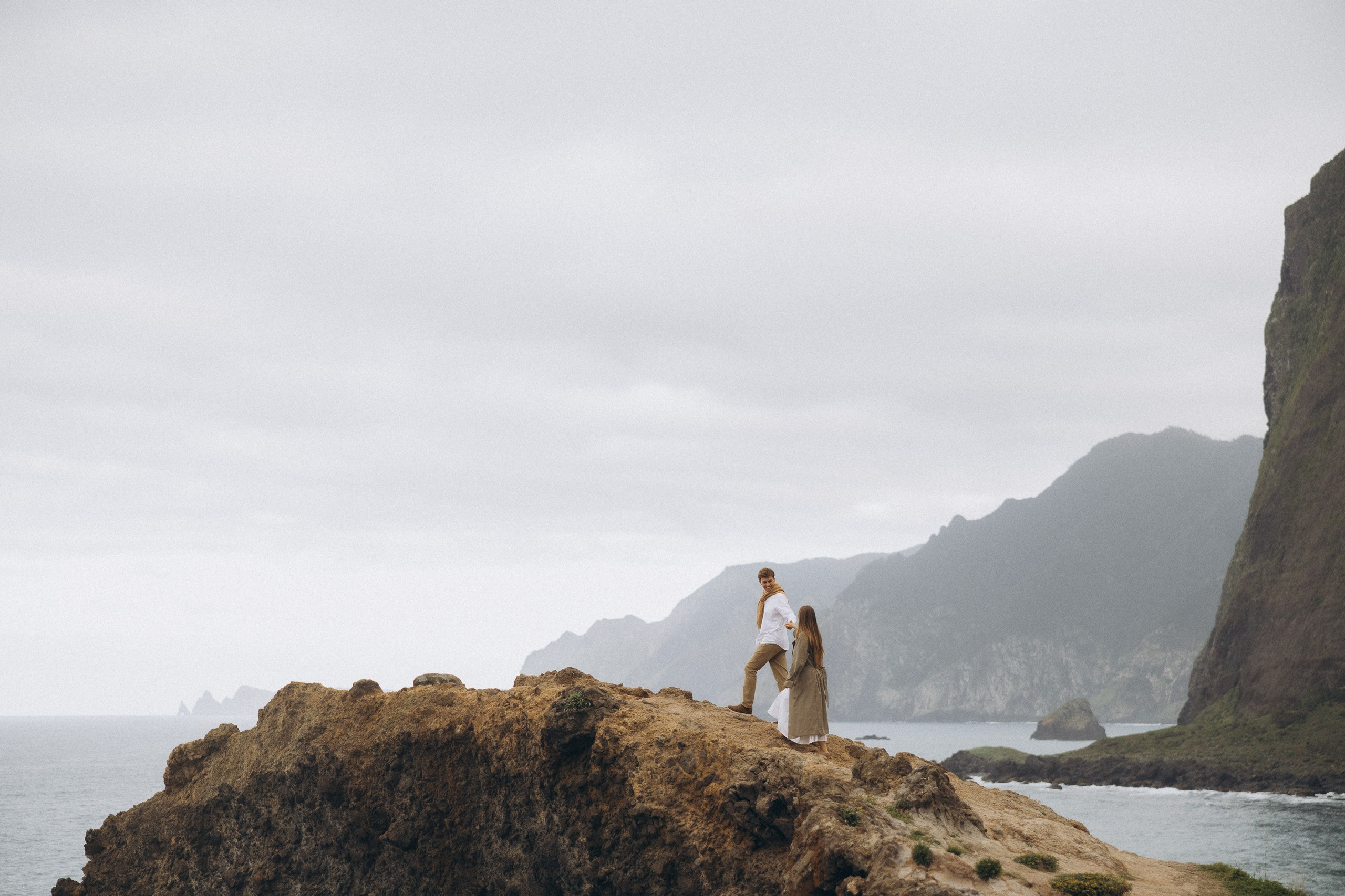 Beautiful engagement moment by the ocean in Madeira, Portugal, as one partner kneels to propose while waves crash in the background.
