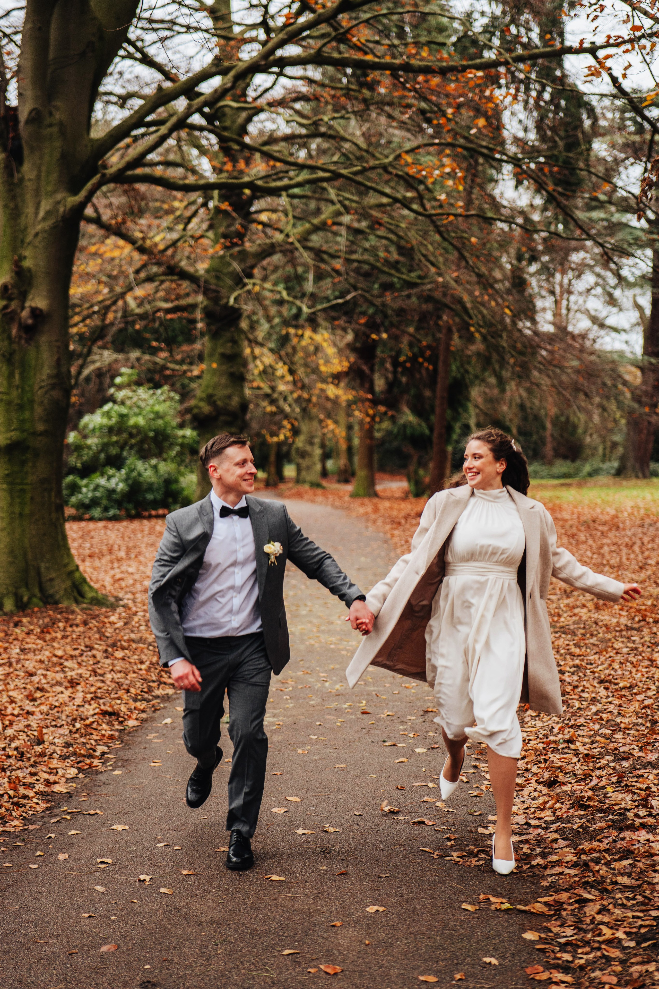 bride and groom running while holding hands in autumn park